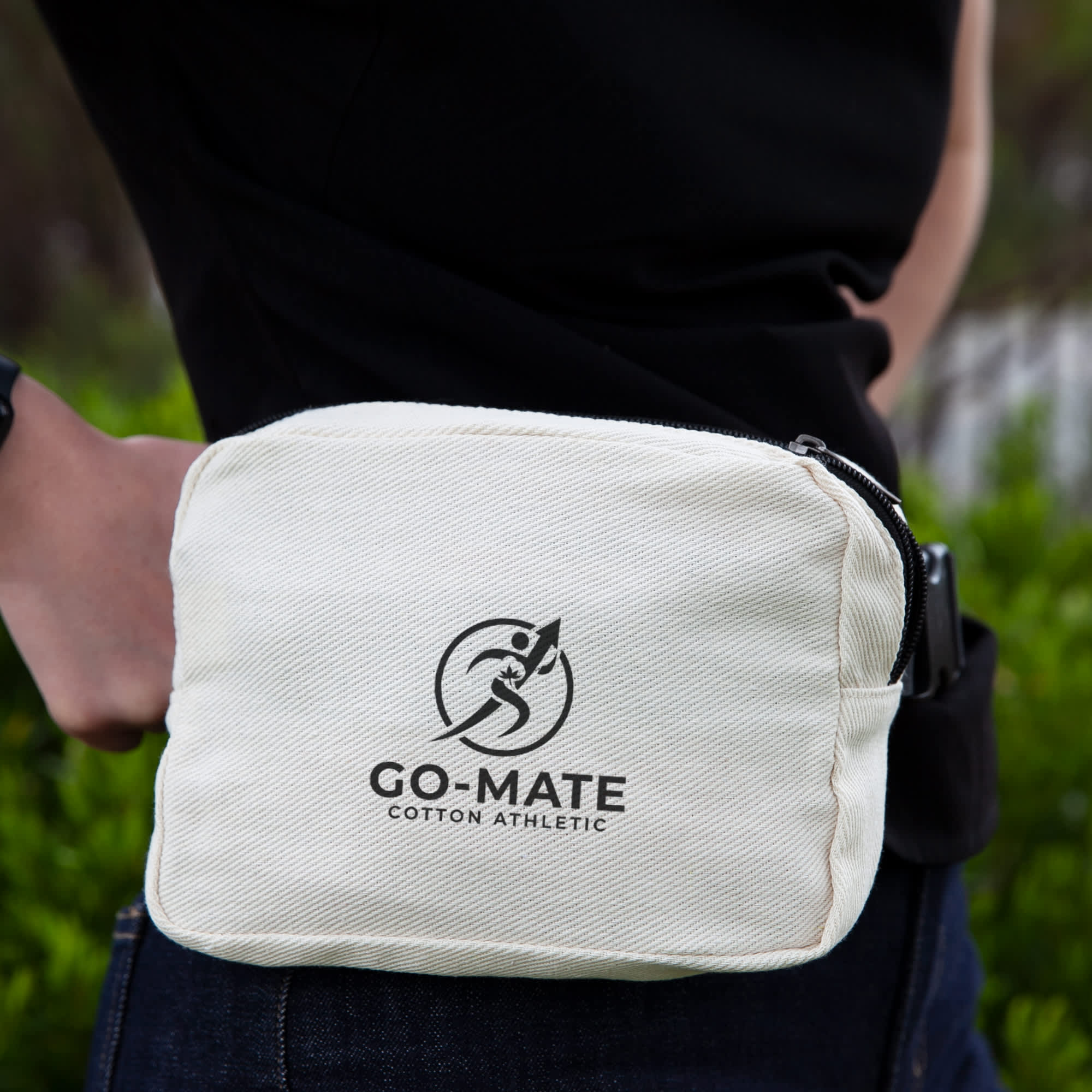A beige cotton belt bag with a logo, worn on the waist against a green background. Go-Mate Cotton Belt Bag - Image 1