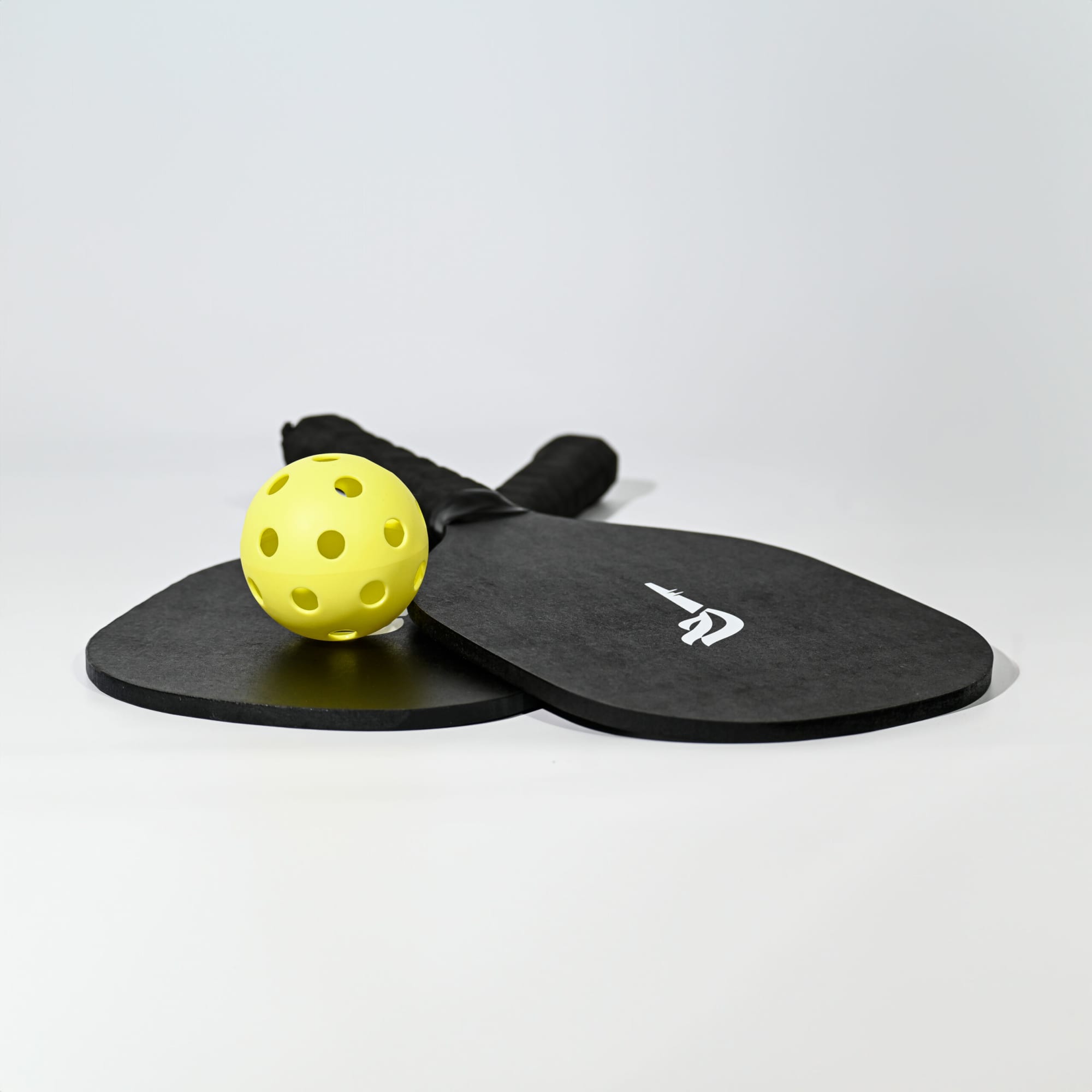 A black pickleball set featuring two paddles and a yellow ball, with a logo on the paddles. Phil's Pickle Ball Set - Image 1