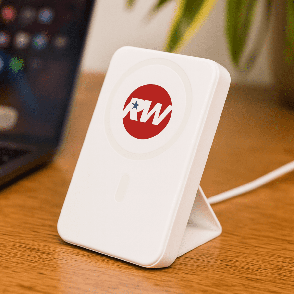 A white wireless charging power bank with a logo, positioned on a wooden surface next to a laptop. Turbo 5000mAh Wireless Charging Power Bank - Image 1