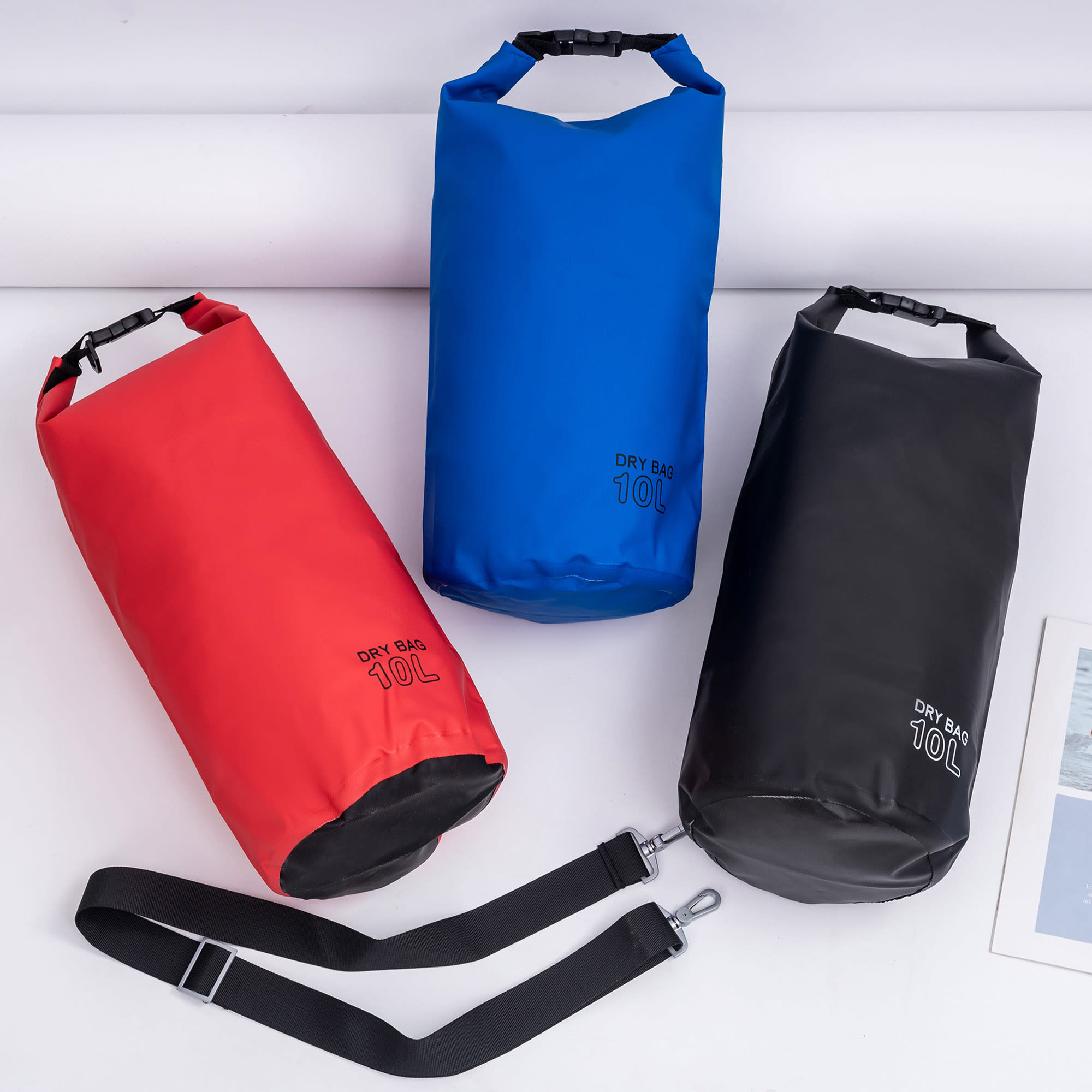 Three dry bags in red, blue, and black, each with a logo and a removable strap. Deluxe Dry Sack – 10L - Image 1