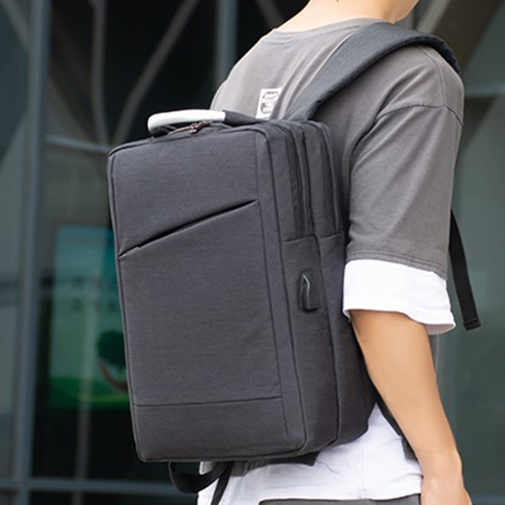 A grey Tokiro laptop backpack is worn on one shoulder, featuring a sleek design and a logo. Tokiro Laptop Backpack - Image 1