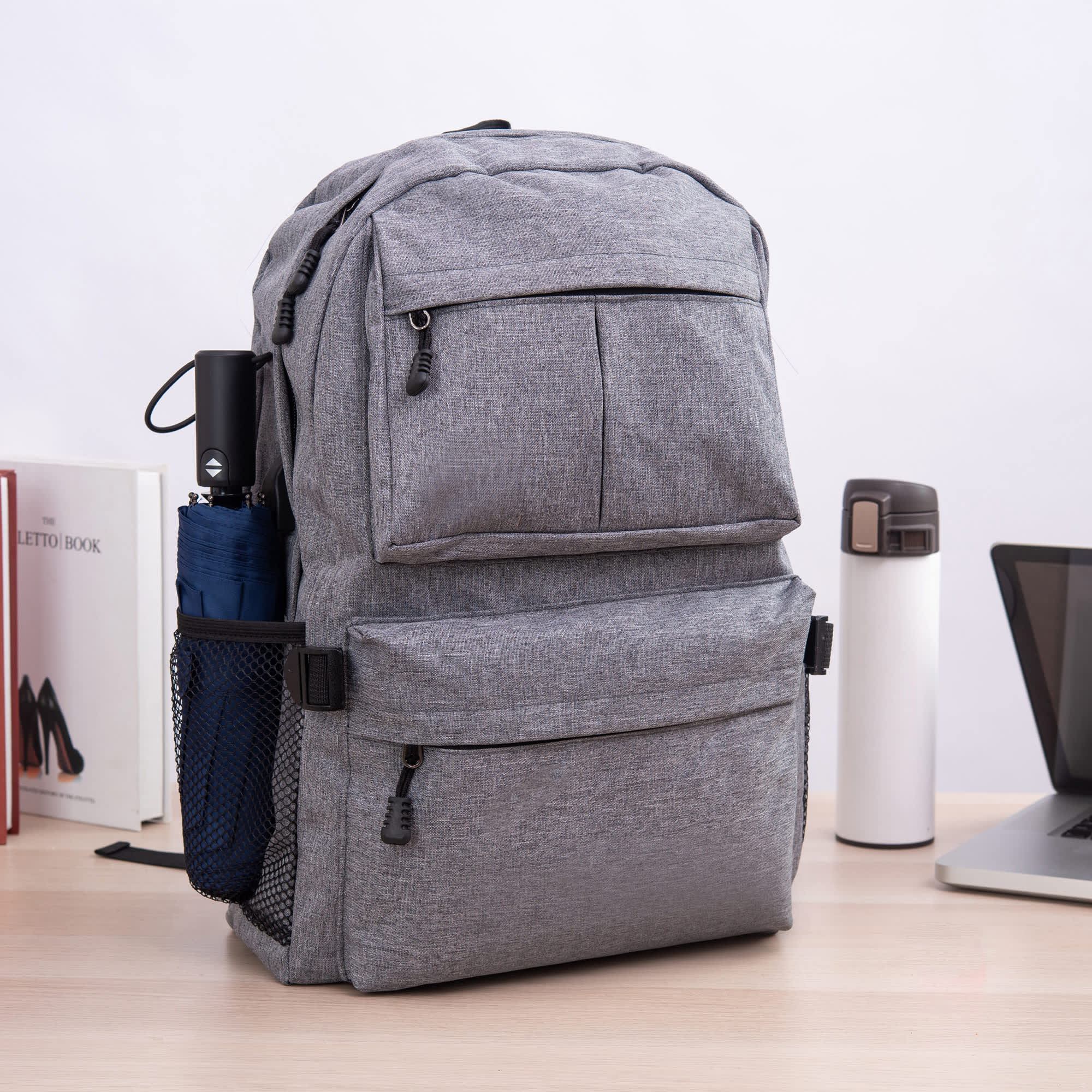 A grey laptop backpack with multiple compartments, side mesh pockets, and a classic design on a desk. Venterna Laptop Backpack - Image 1