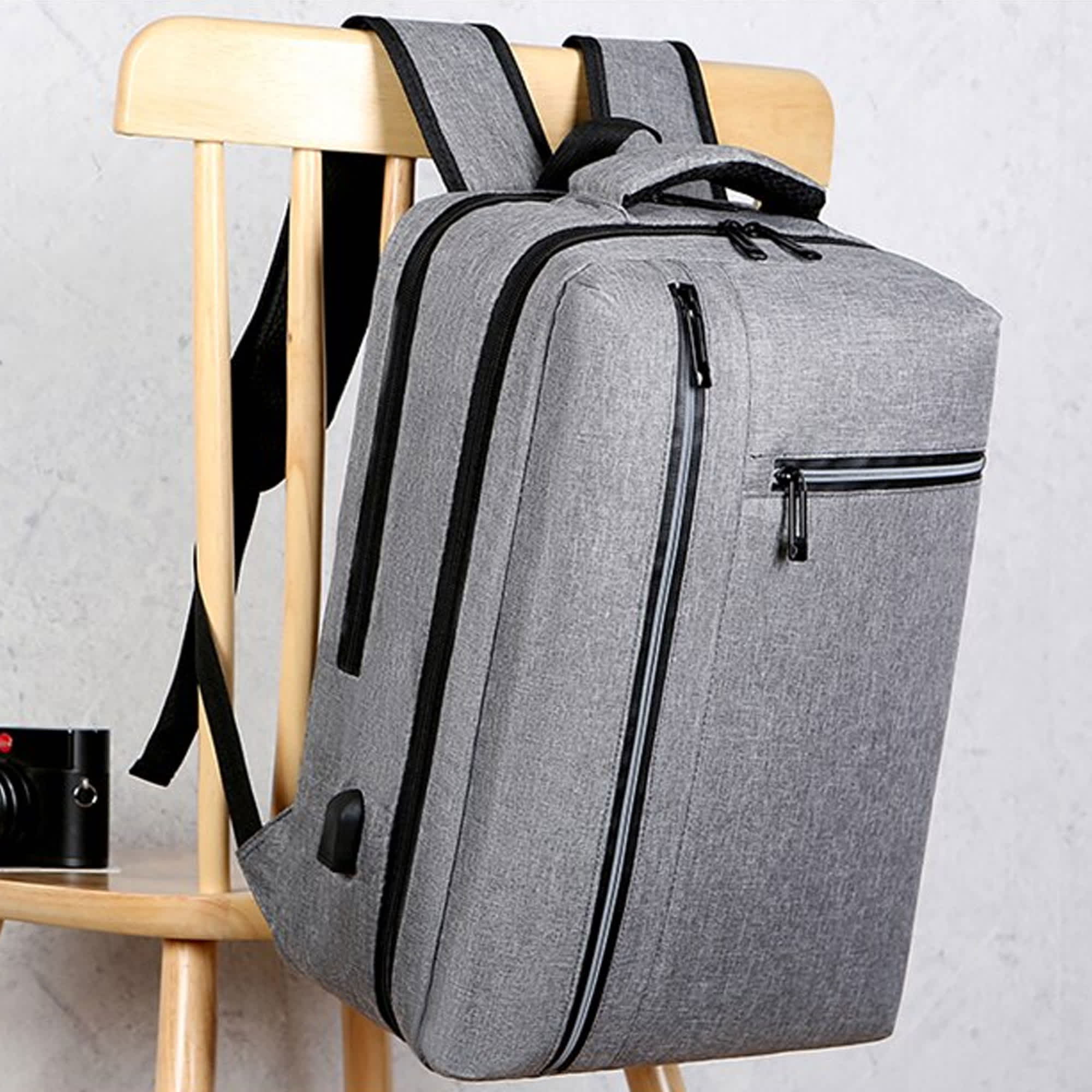 A sleek grey laptop backpack with multiple compartments hanging on a wooden chair. It features a logo on the side. Misty Laptop Backpack - Image 1