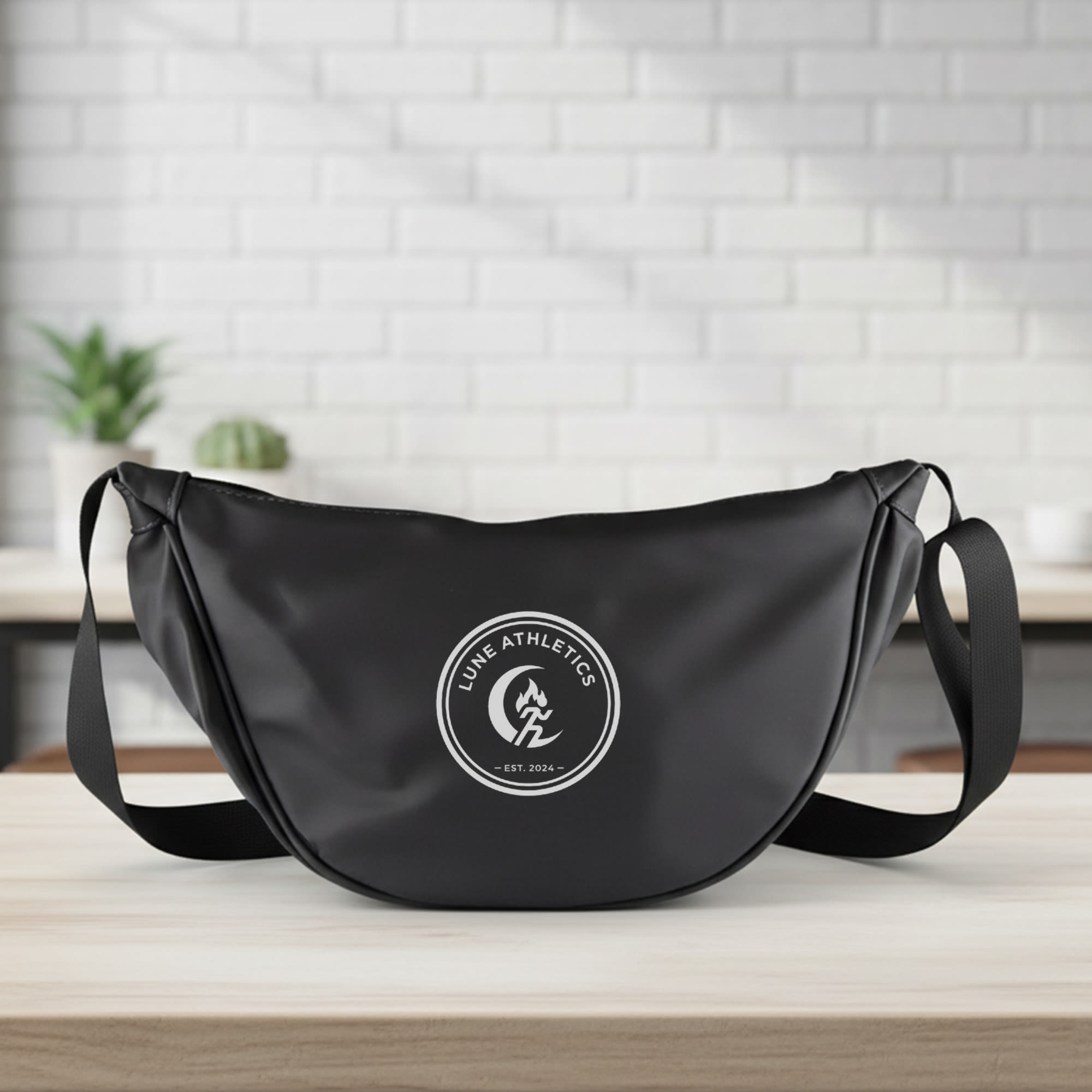 A black promotional bag with a round logo, featuring a single strap for wearing crossbody. The Lune Bag - Image 1