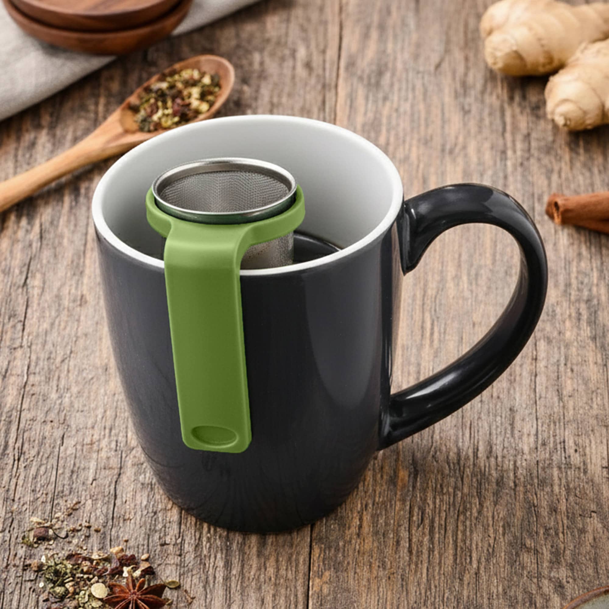 A drink bottle with a black exterior and green tea infuser sits in a mug, surrounded by loose tea and spices. Travel Tea Infuser - Image 1