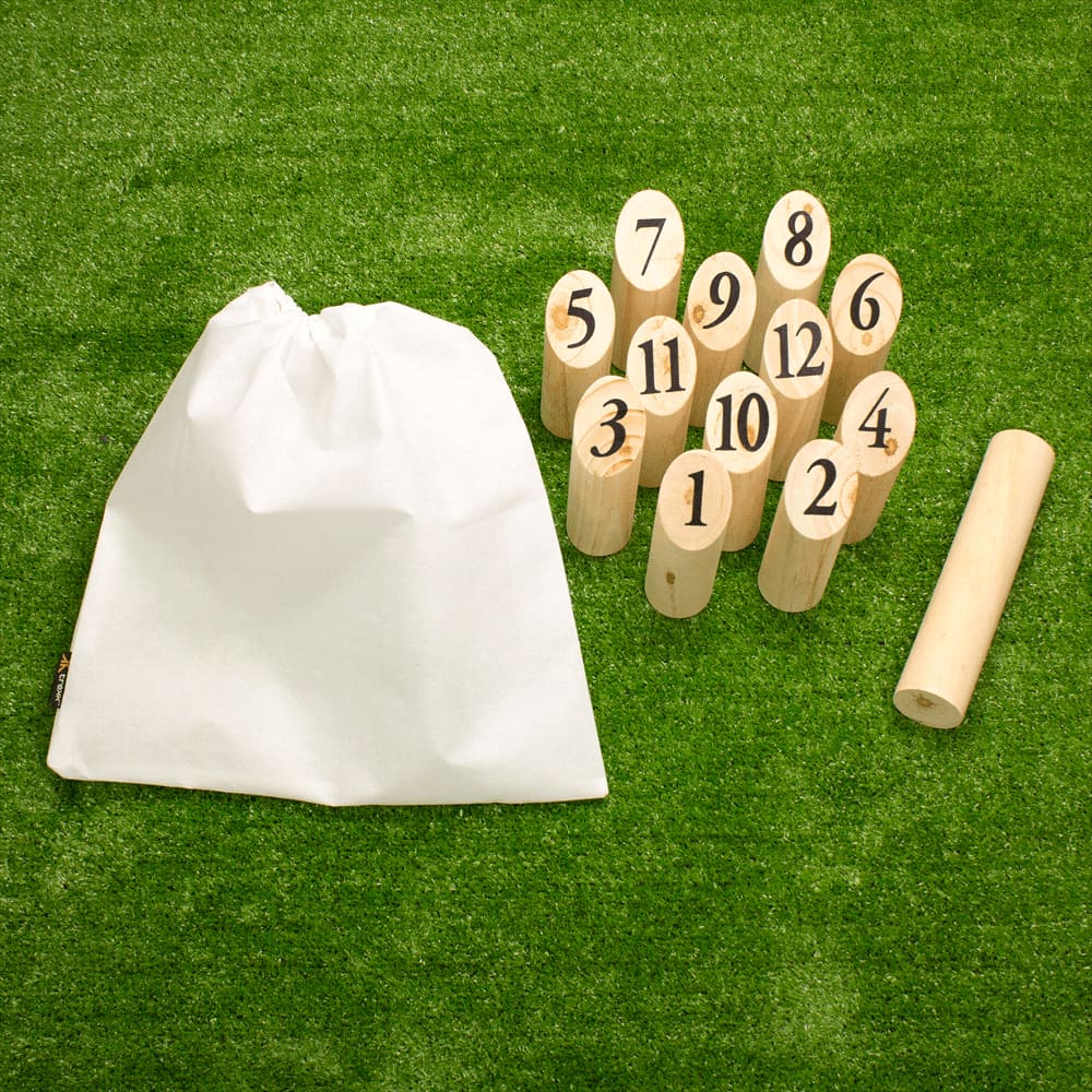 A set of wooden skittles with numbers, a throwing stick, and a white drawstring bag, arranged on grass. Trekk Skittle Throw Game - Image 1