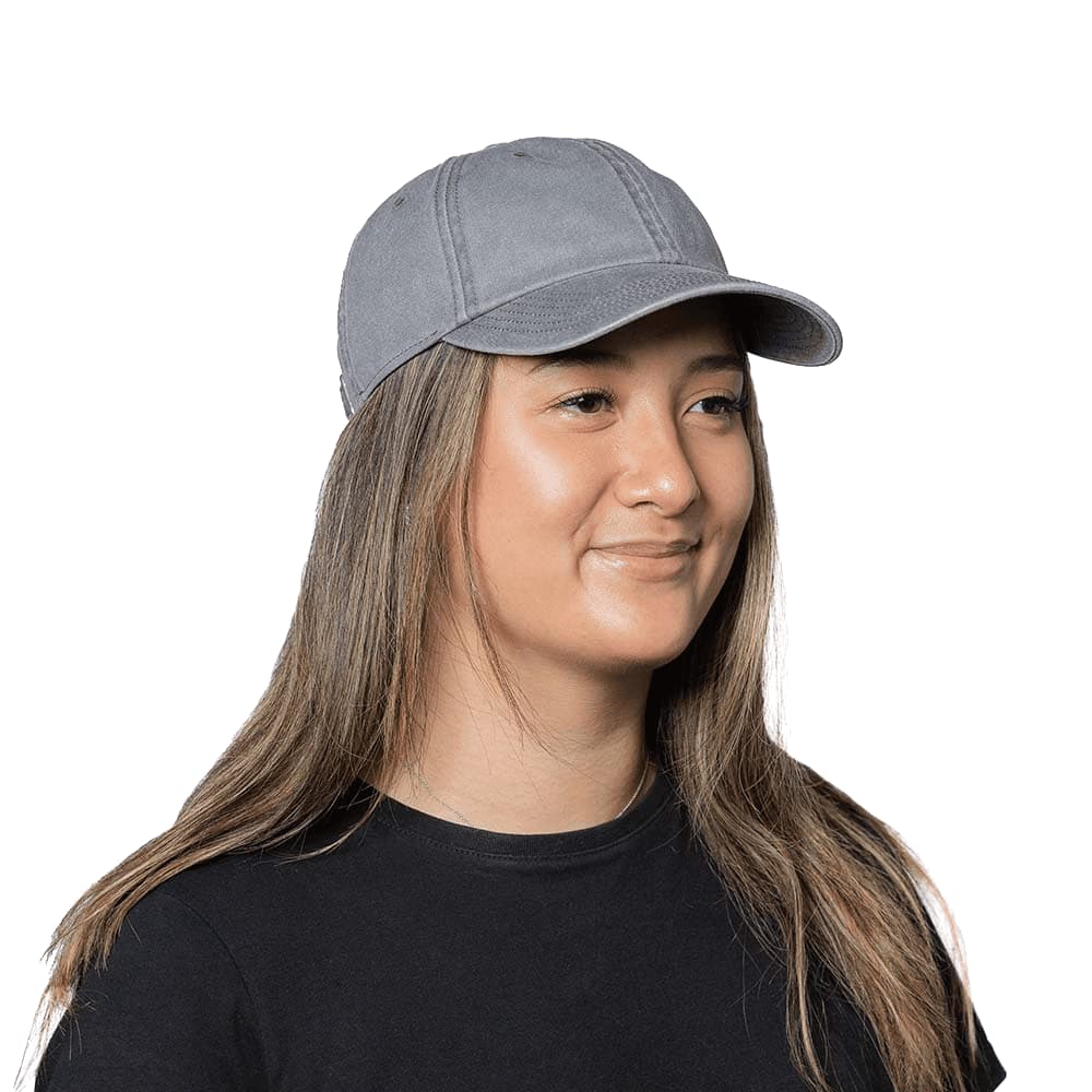 A grey organic washed cotton cap with a curved brim, worn by a woman with long hair. The cap includes a logo. Trekk Austin Organic Washed Cotton Cap - Image 1