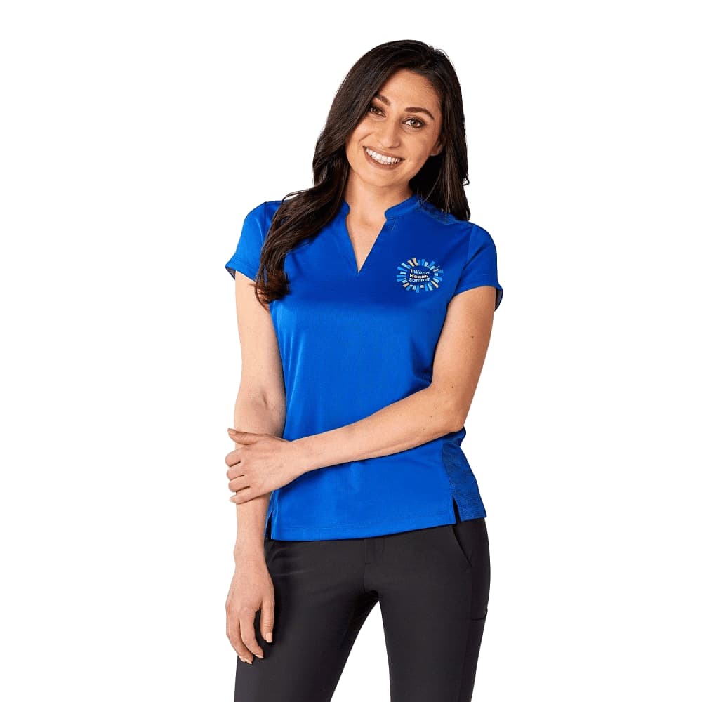 A woman is wearing a vibrant blue short sleeve performance polo shirt with a logo on the chest. Women's Piedmont Short Sleeve Performance Polo - Image 1