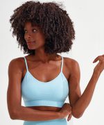 A light blue sport bra with seamless design and thin straps, featured on a model with curly hair and a neutral background.