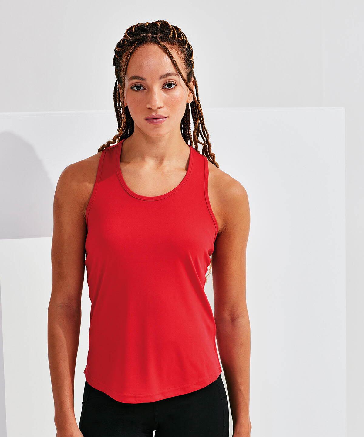 A red slim racerback vest, made from recycled materials, displayed on a model with braided hair. A red slim racerback vest, made from recycled materials, displayed on a model with braided hair.