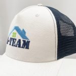 A custom trucker cap featuring a beige front and navy blue mesh back, with a logo on the front.