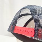 A custom trucker cap featuring a black mesh back and a vibrant red adjustable strap. It has a logo on the front.