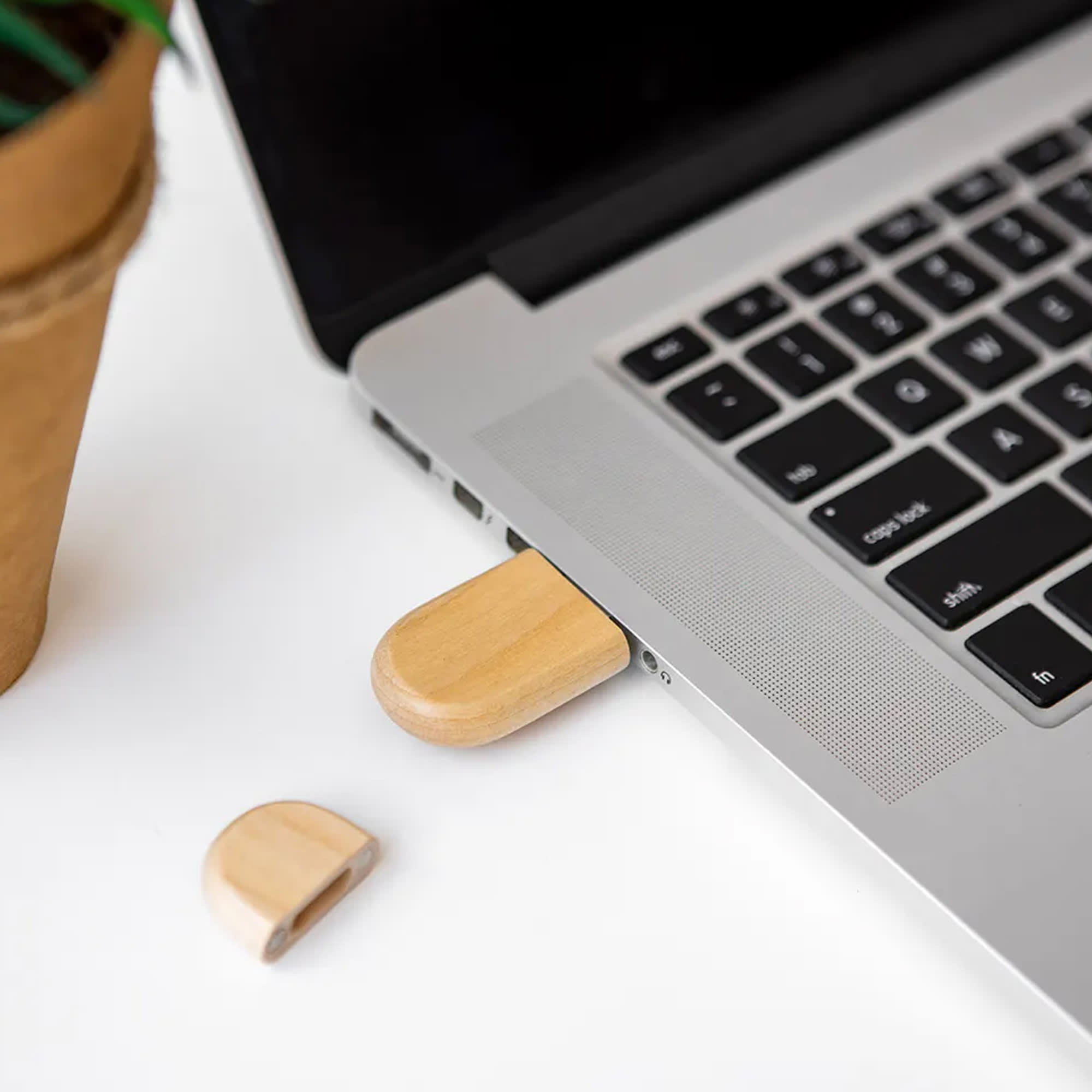 A bamboo USB flash drive is plugged into a laptop, with a cap resting beside it on a white surface. Okoolar Bamboo USB 16GB - Image 1