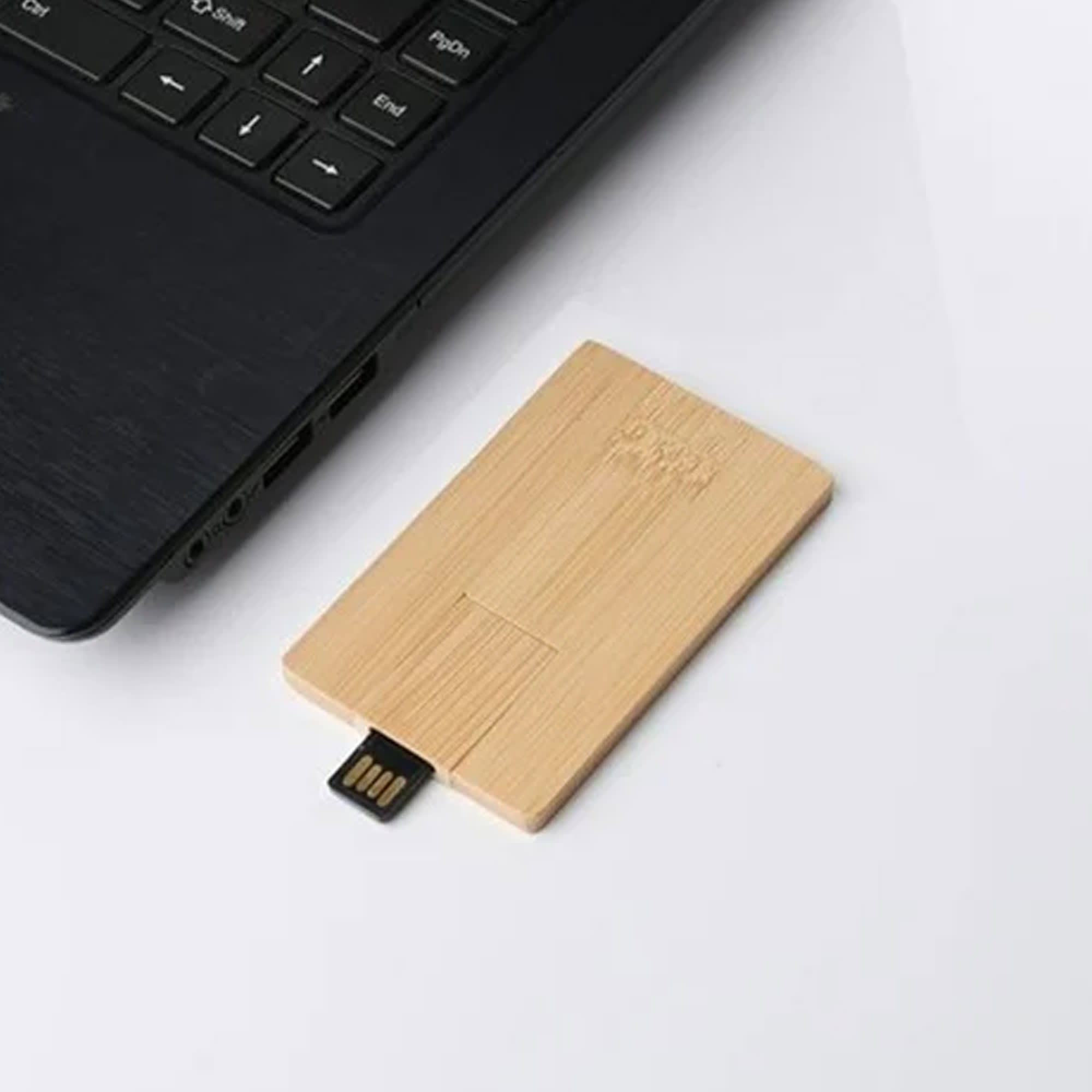 A bamboo USB flash drive in a rectangular shape, resting beside a laptop on a white surface. It features a branding logo. Ultra Bamboo USB 16GB - Image 1