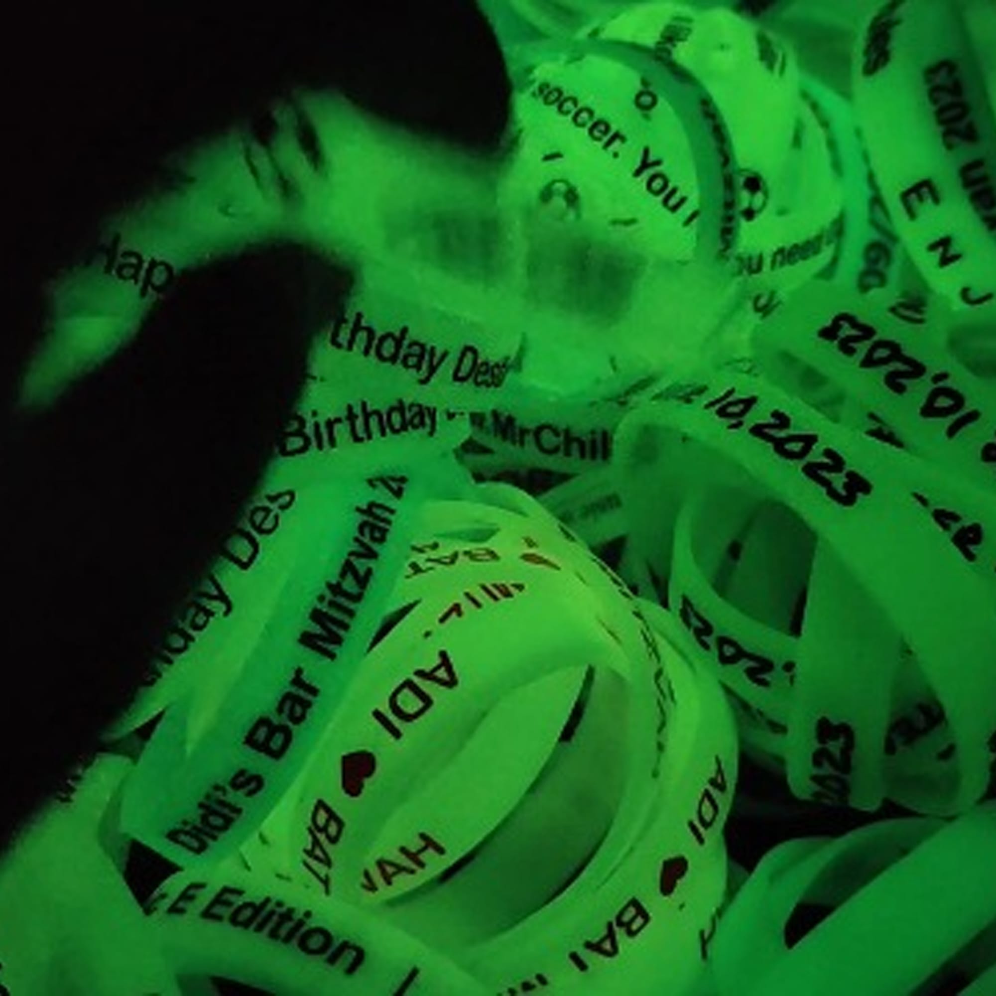 A collection of neon green silicone wristbands with various printed messages, glowing in the dark. Neon Glow Silicone Wrist Band - Image 1