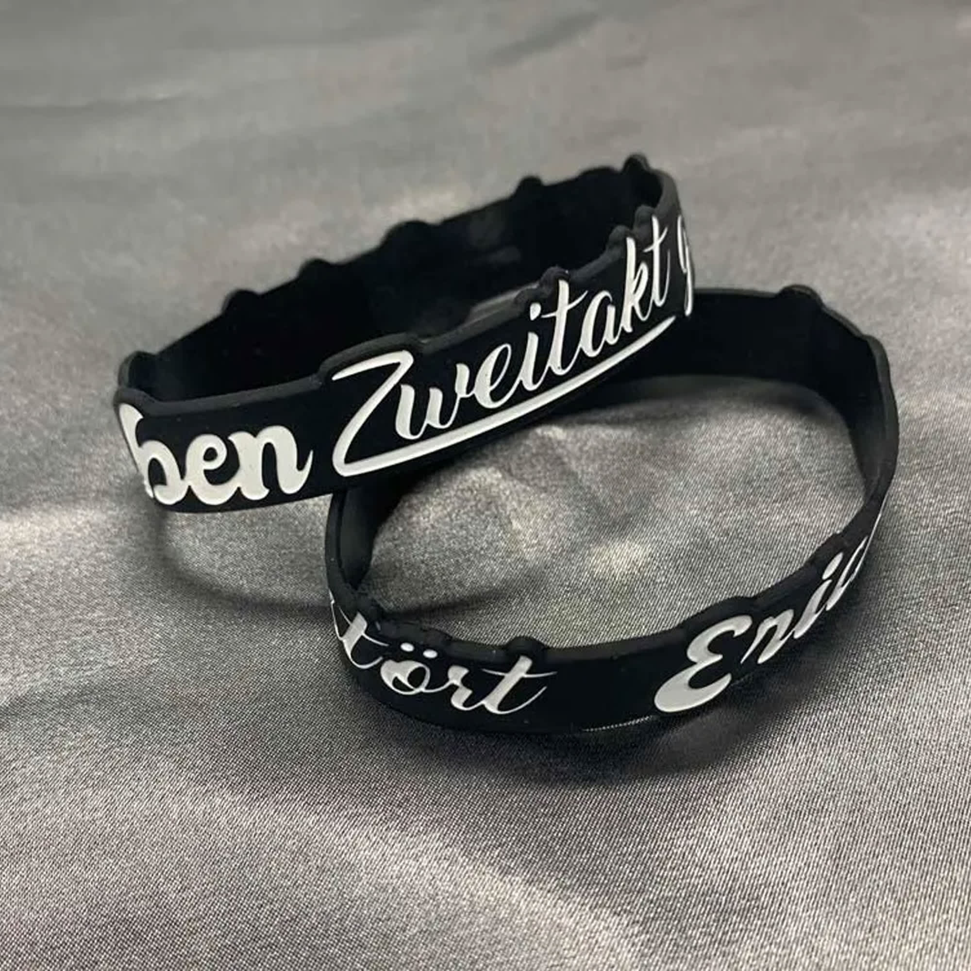 Two black silicone wristbands featuring white custom designs, displayed on a grey background. Toaks Silicone Wrist Band Custom Design - Image 1