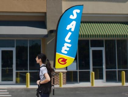 A small single-sided backpack wing banner in blue and yellow, attached to a person walking near a store. Small Single Sided Backpack Wing Banner - Image 1