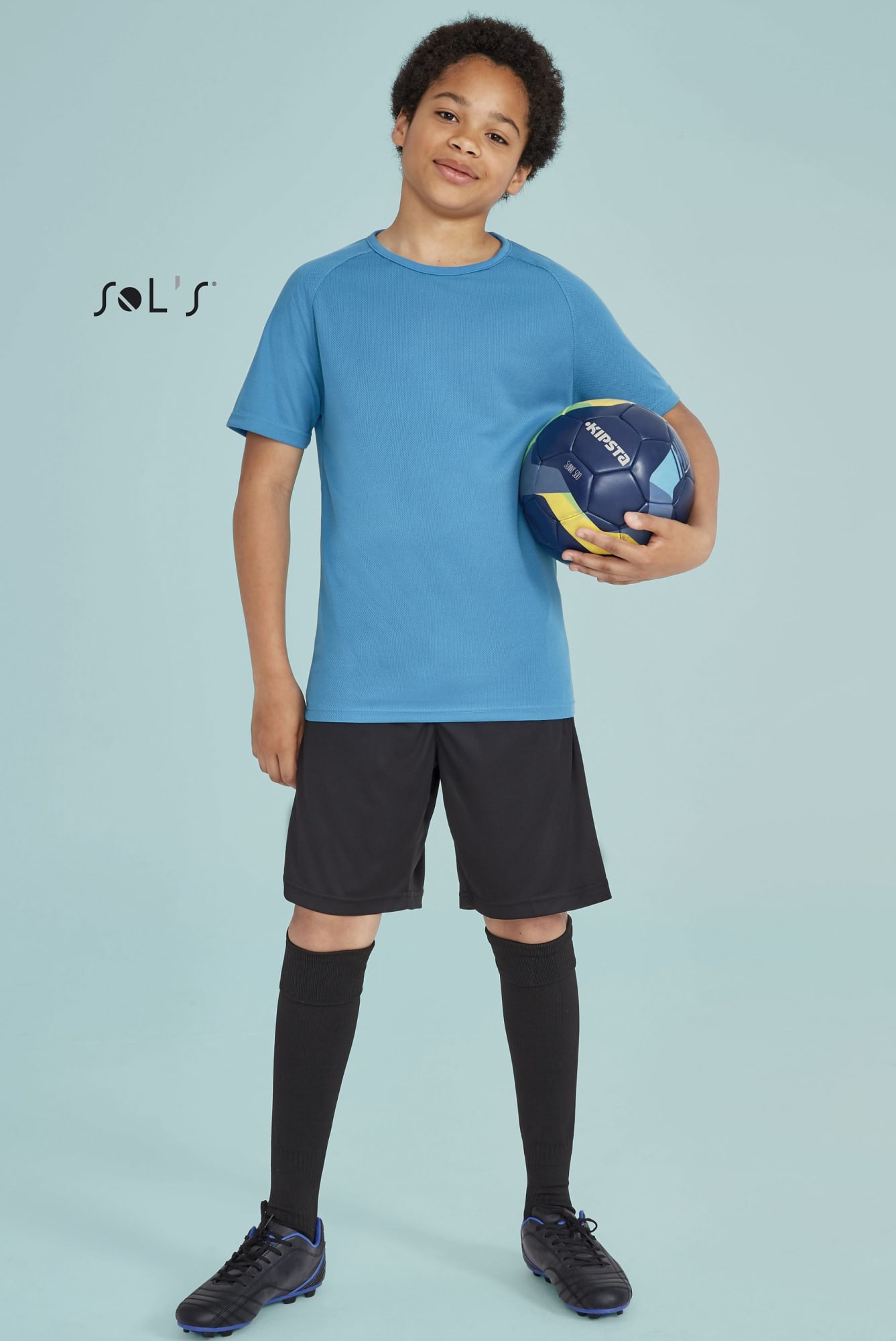 A boy stands holding a blue sport ball, wearing a blue breathable polyester T-shirt, black shorts, and black socks. T shirt KIDS 100% breathable polyester SPORTY - Image 1