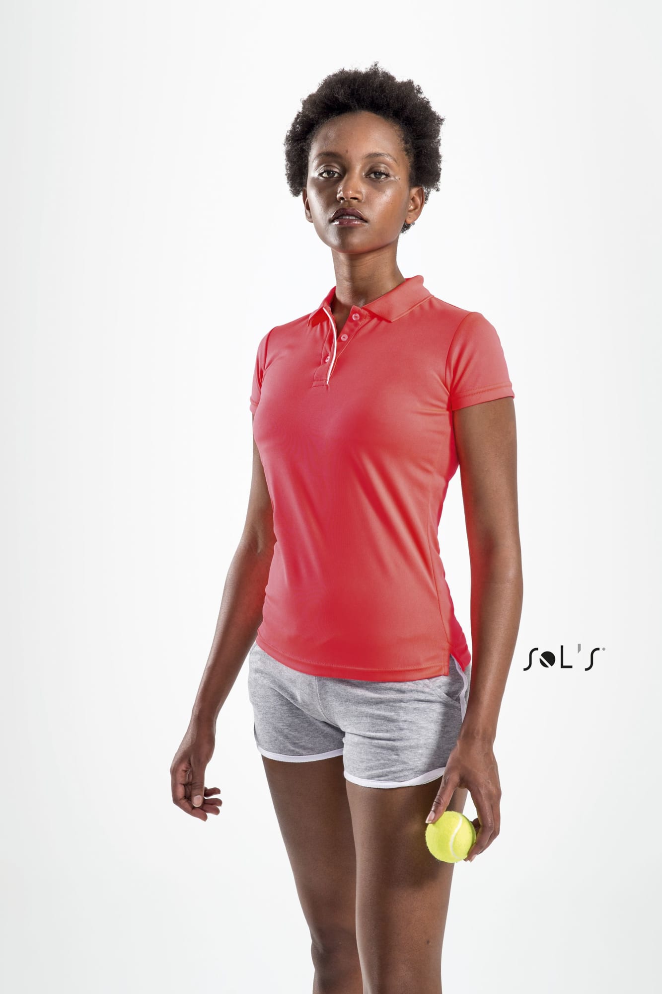 A woman wearing a pink polo shirt and grey shorts, holding a tennis ball, with a plain background. Polo shirt women's sports polyester PERFORMER - Image 1