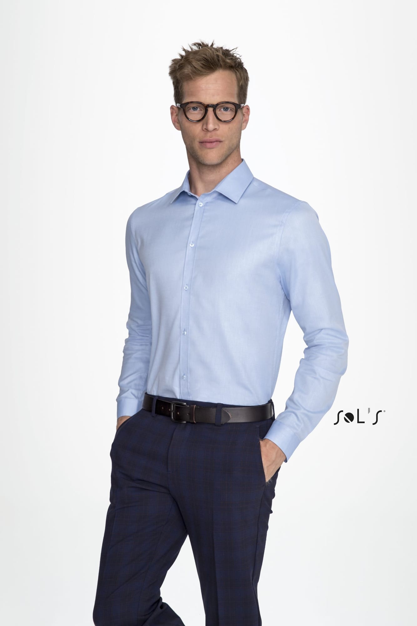 A long-sleeve light blue herringbone shirt worn by a man with glasses, paired with dark trousers. It features a logo. Business shirt BRODY MEN'S - HERRINGBONE SHIRT Long sleeve - Image 1