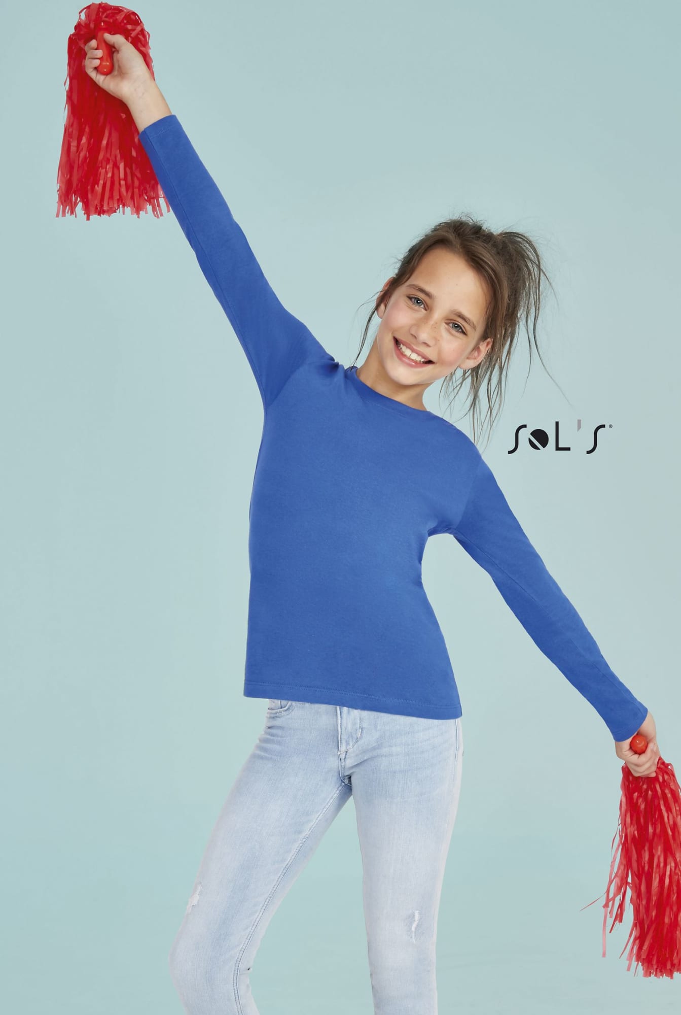 A bright blue long sleeve T-shirt made from 100% semi combed ring spun cotton, worn by a smiling girl with red pom-poms. T-shirt Long sleeve kids 100% semi combed ring spun cotton IMPERIAL - Image 1