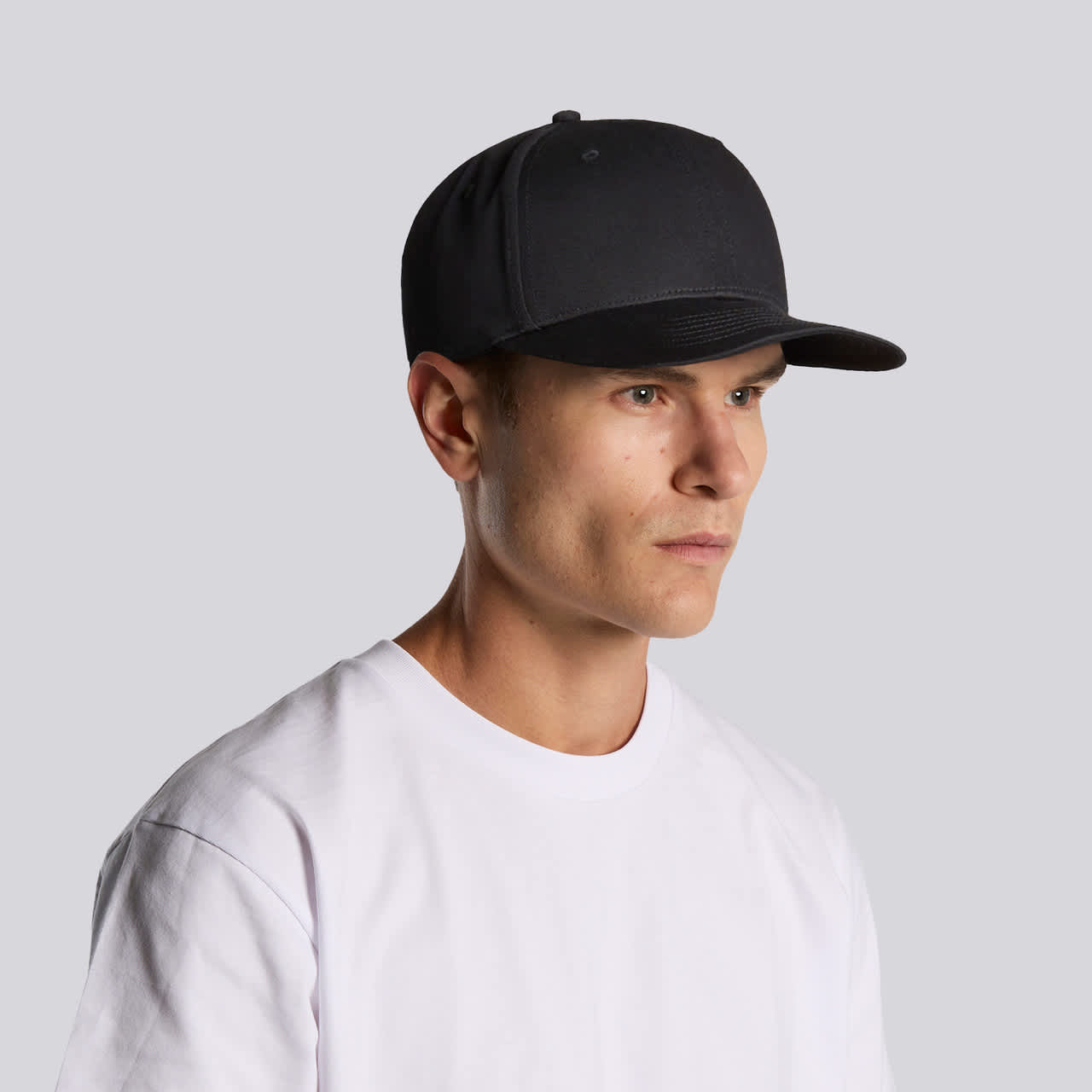 A black cap with a structured design, featuring a curved brim and a logo on the front, worn by a young man. Stock Flex Cap - Image 1