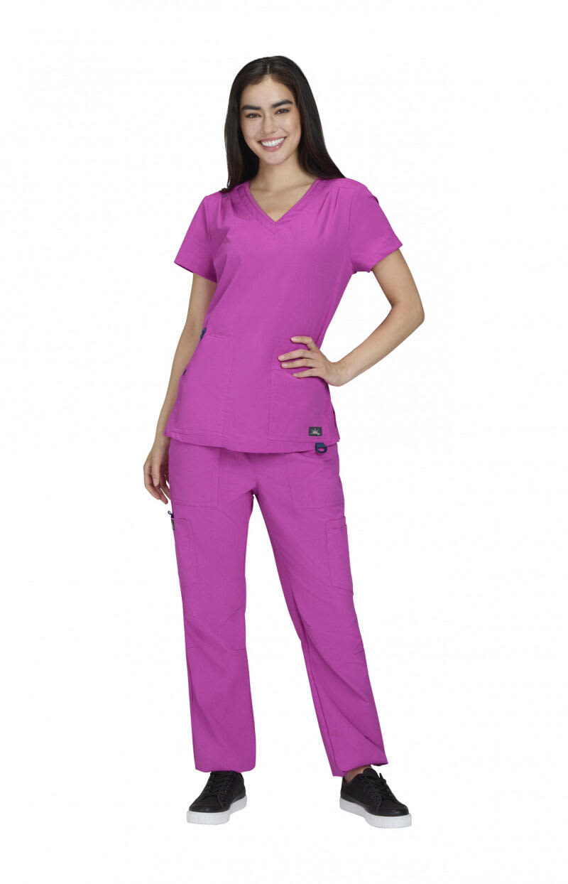 A woman wears a bright pink Sari Top scrub set, consisting of a V-neck top and matching trousers, with a logo present. Sari Top - Image 1