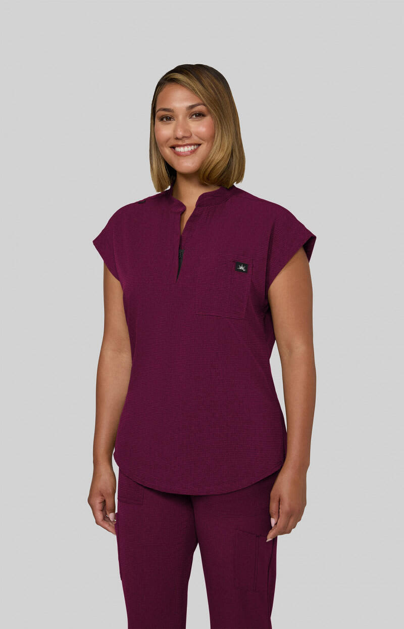 A purple scrub top with a collar and cap sleeves, featuring a logo on the chest. Catrin Top - Image 1