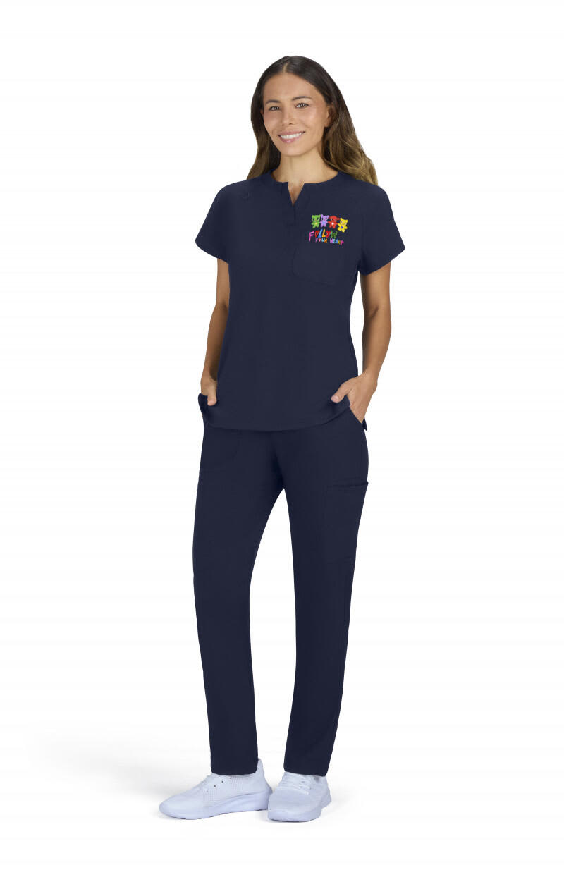 A woman wearing a navy placement top and matching pants, with pockets and a colourful logo on the top. Hope Bloom Placement Top - Image 1