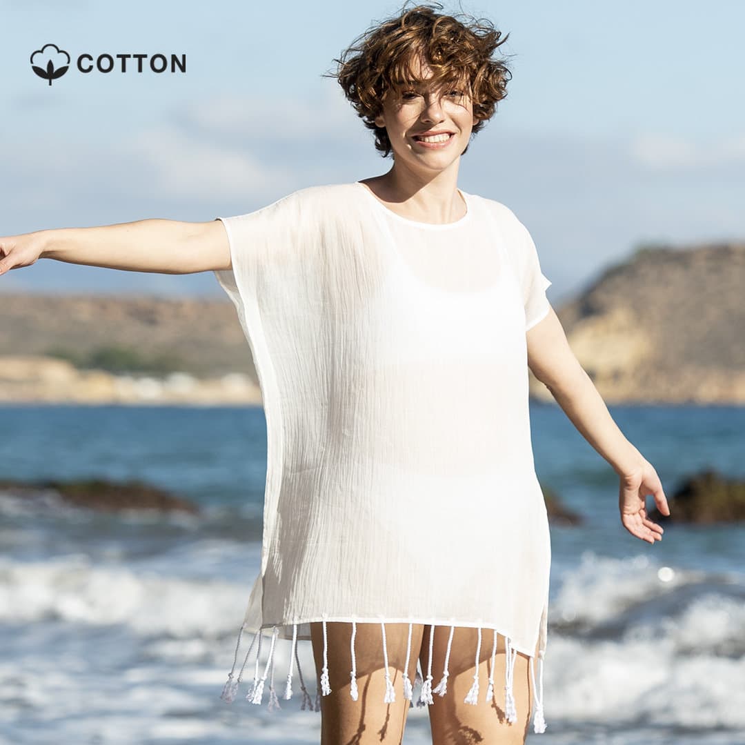 A lightweight, white kaftan with tassels, designed for summer wear, standing against a beach backdrop. Roseux Kaftan - Image 1