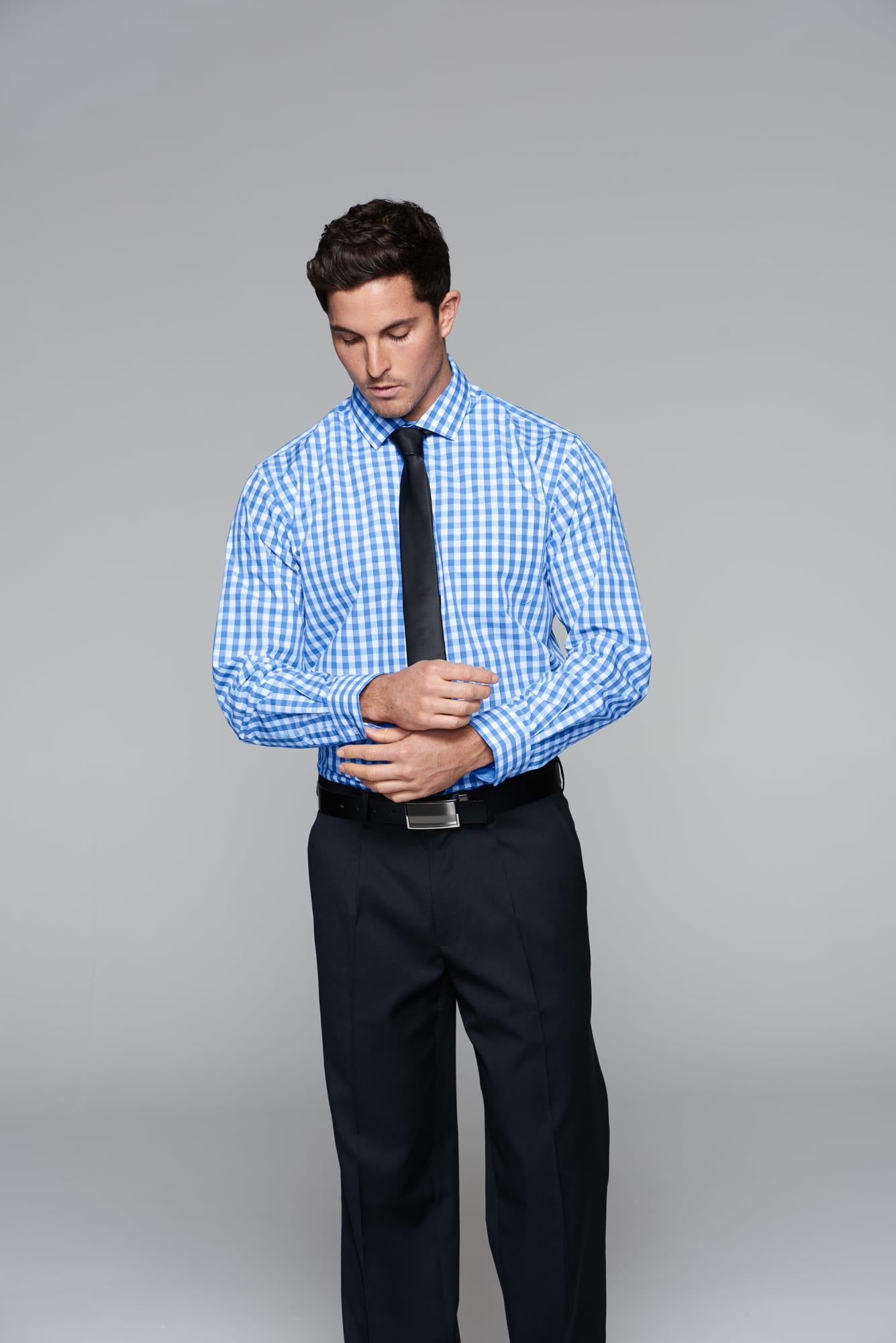 A button-up long sleeve shirt in blue and white check pattern, paired with black pants and a tie, with a logo visible. DEVONPORT MENS SHIRT LONG SLEEVE RUNOUT - Image 1