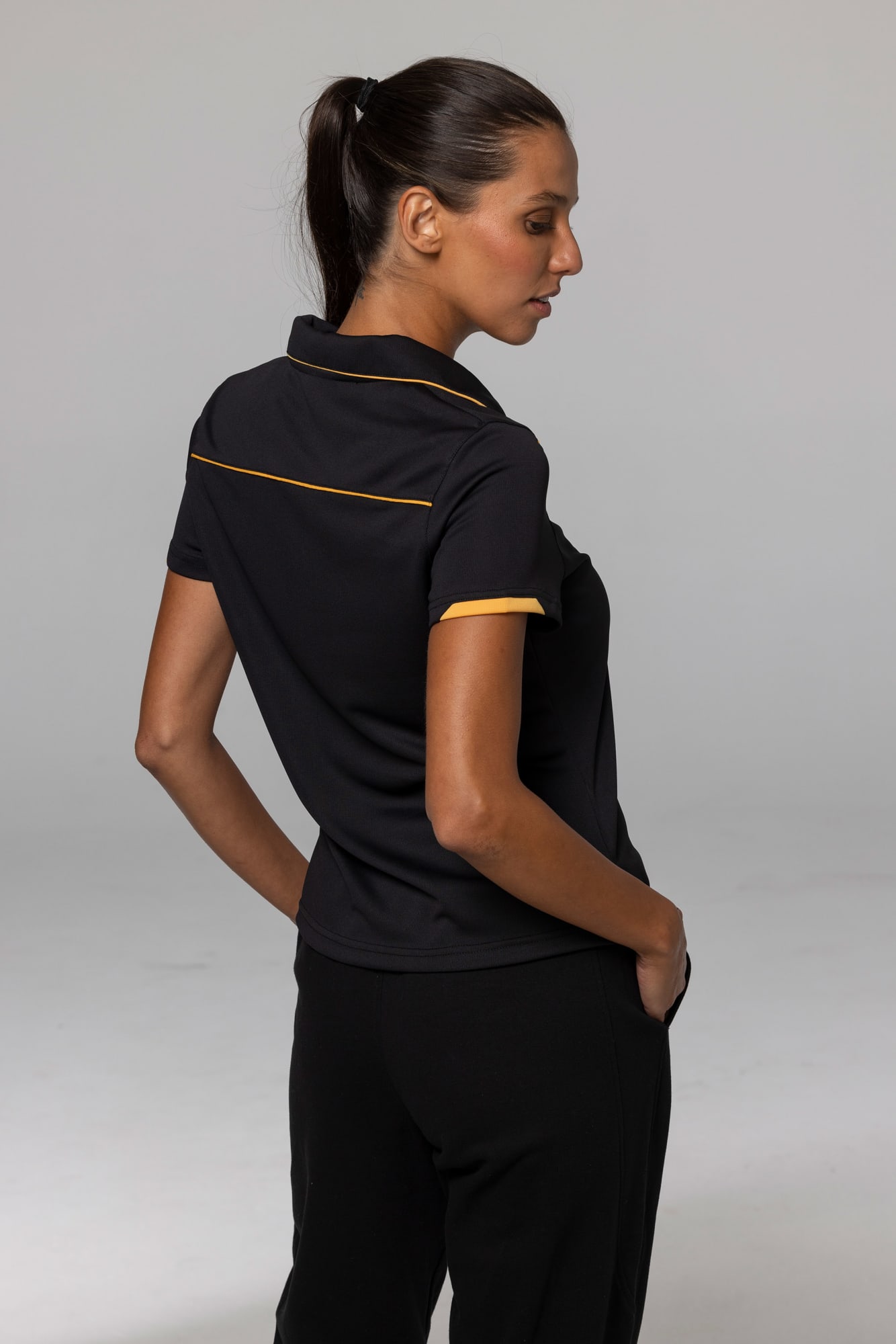 A black polo shirt with contrasting yellow accents, featuring a collar and logo. CURRUMBIN LADY POLOS - Image 1