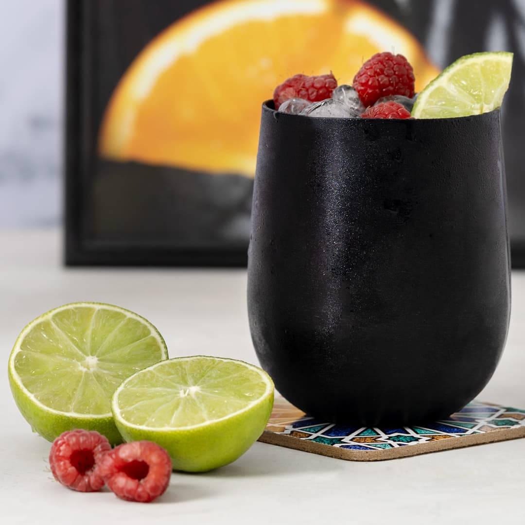 A drink bottle in a sleek black design, filled with ice, raspberries, and lime slices, alongside halved limes. Amely - Image 1