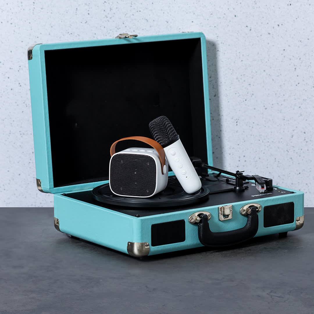 A turquoise karaoke speaker in a suitcase design, accompanied by a microphone, on a grey surface. Sophie Karaoke Speaker - Image 1