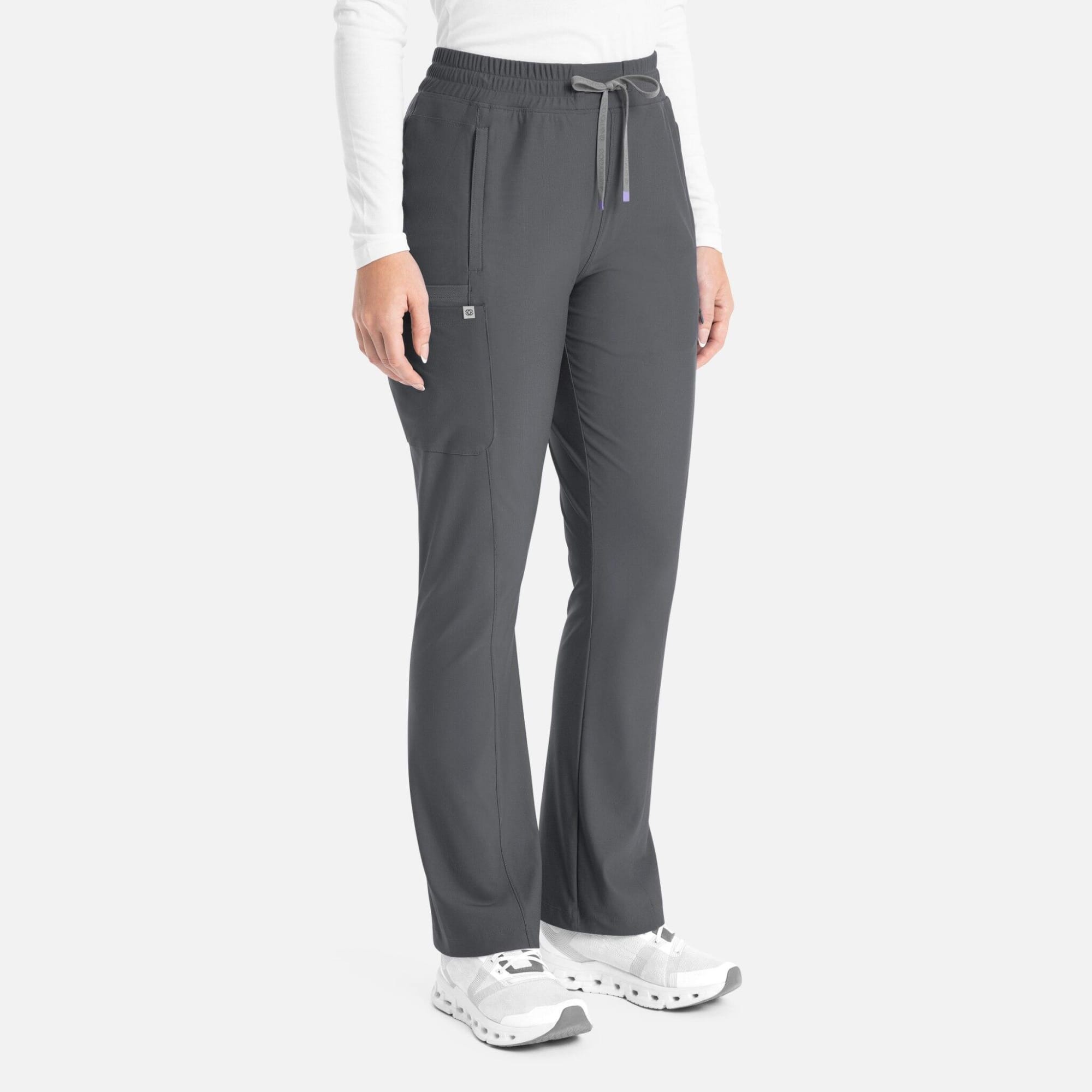 A woman is wearing dark grey bootcut pants with an elastic waistband and pockets, paired with white shoes. Embrace Nora Bootcut Pant - Image 1