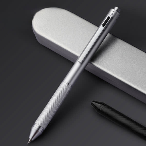 A silver 4-in-1 ballpoint pen sits atop a sleek grey case, featuring a textured grip and a black pen nearby. 4-in-1 Colored Ball Point Pen - Image 1