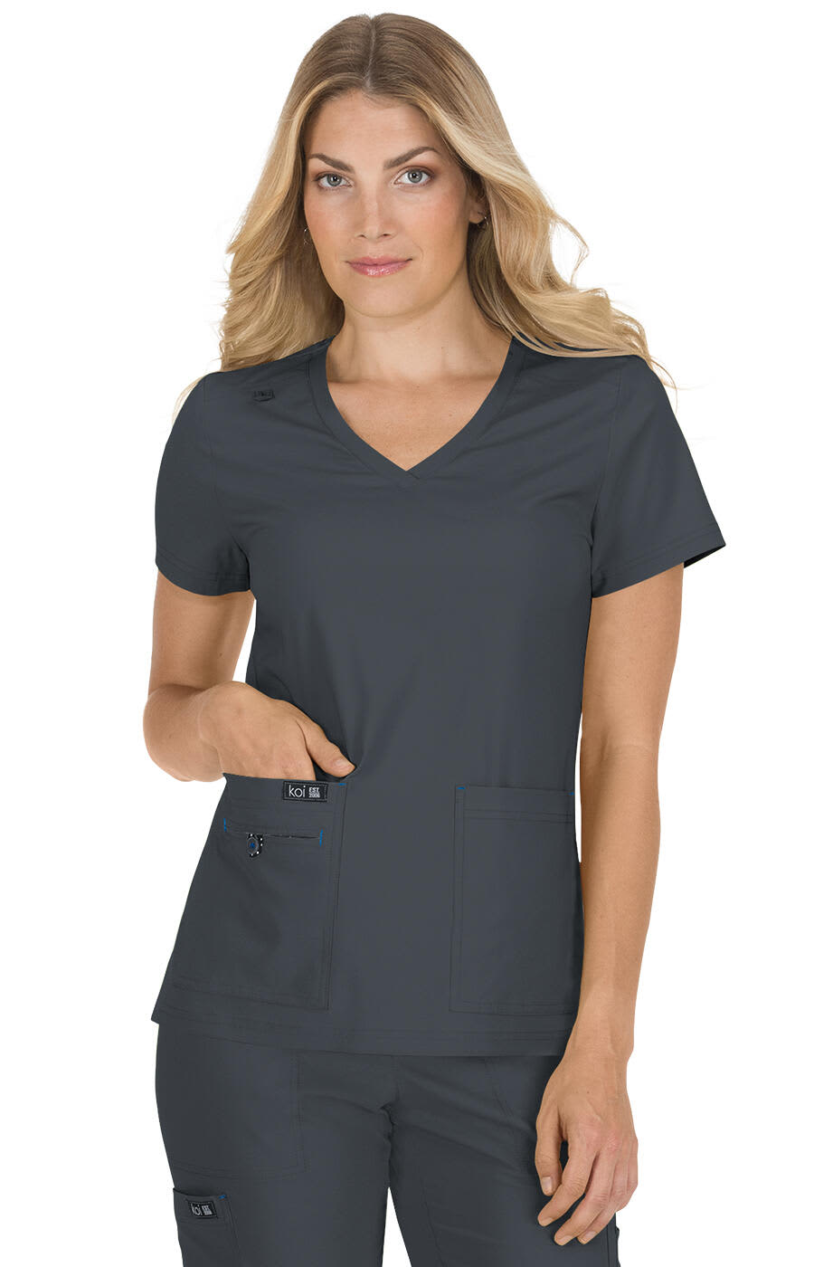 A grey scrubs top with a V-neck, featuring short sleeves and two front pockets, worn by a model. Becca Top - Image 1