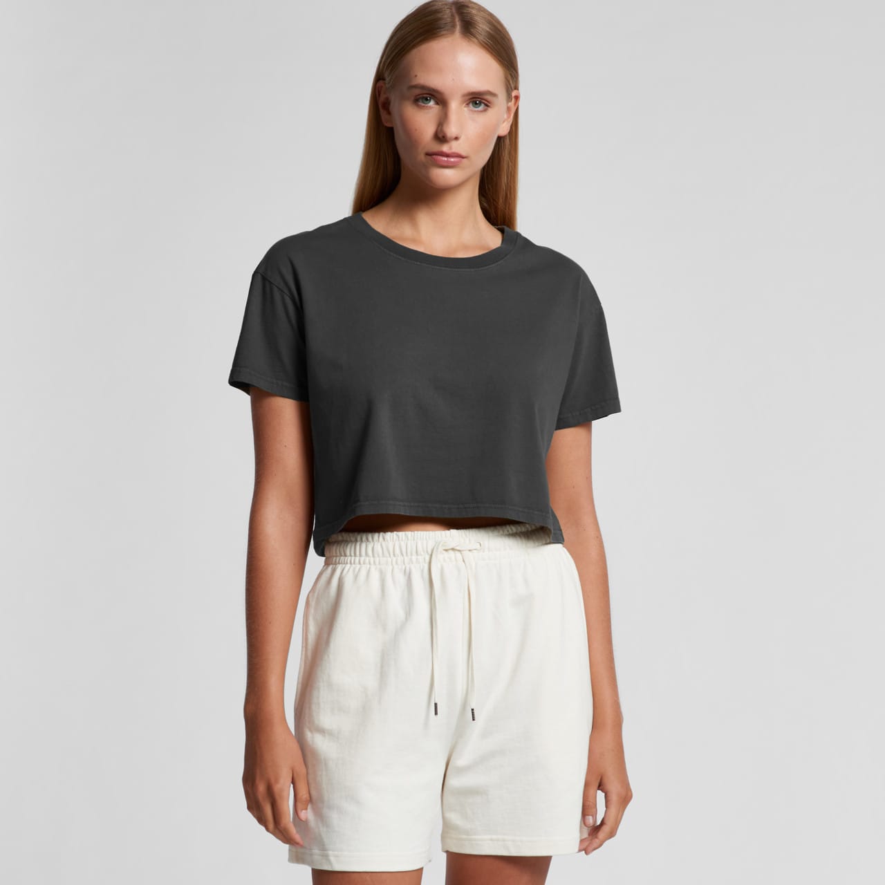 A cropped black T-shirt is paired with white shorts. The model stands against a neutral background. Wo's Faded Crop Tee - Image 1