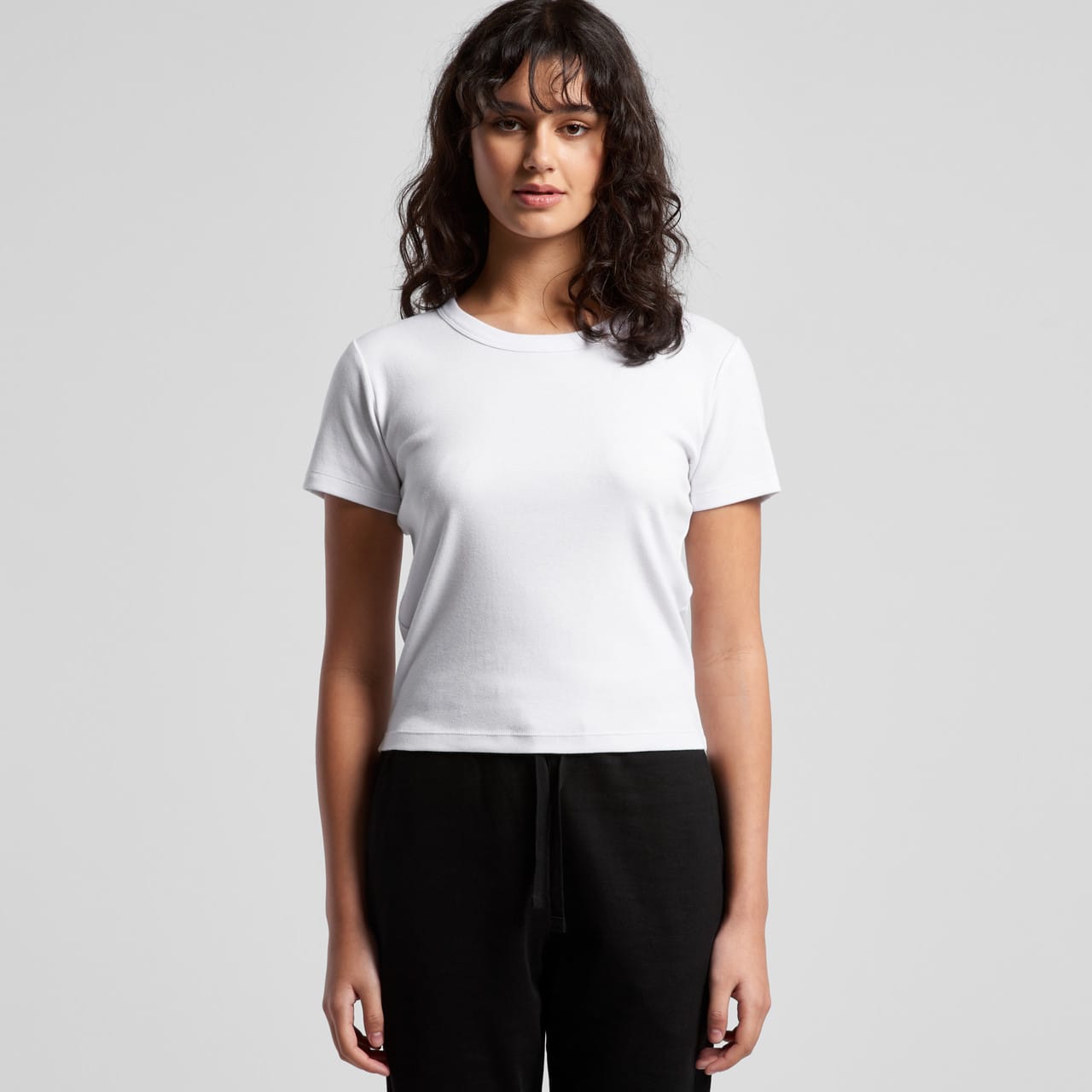 A white, short-sleeved baby tee with a fitted design. The model stands against a plain background. Wo's Organic Rib Baby Tee - Image 1