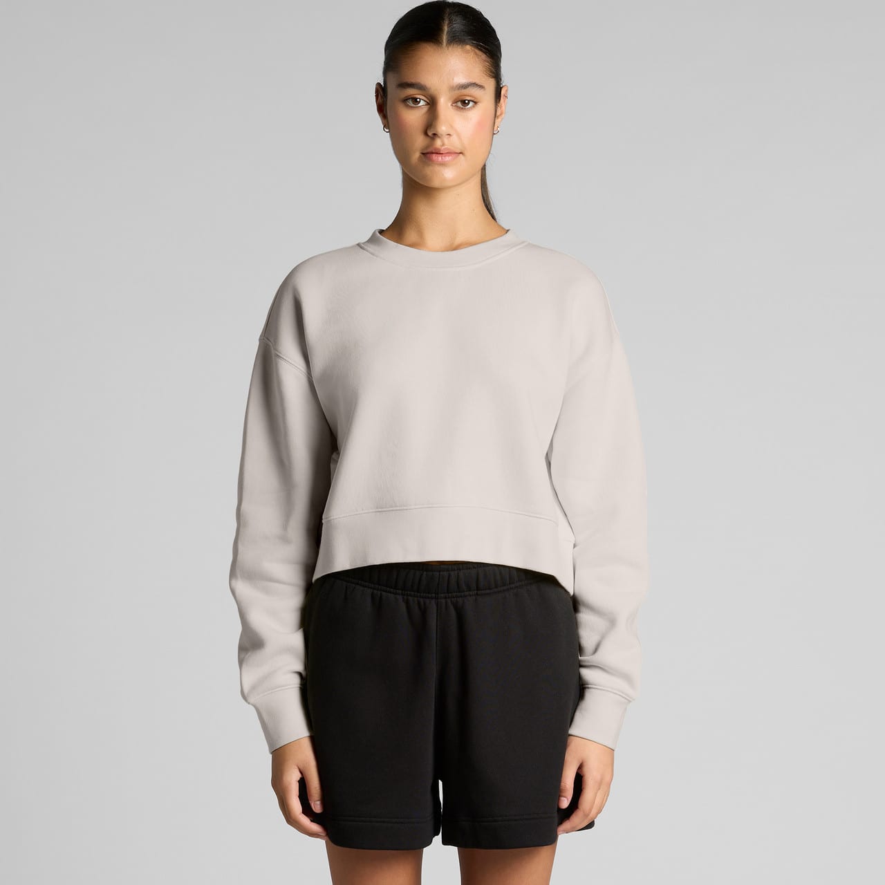A light grey cropped jumper with a relaxed fit, paired with black shorts, featuring a branding logo. Wo's Relax Crop Crew - Image 1