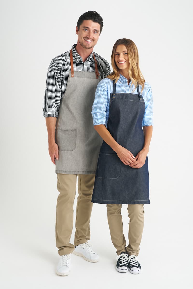 A grey bib apron and a navy bib apron are worn by two models, both with logos and casual outfits. Byron - Bib Apron - Image 1