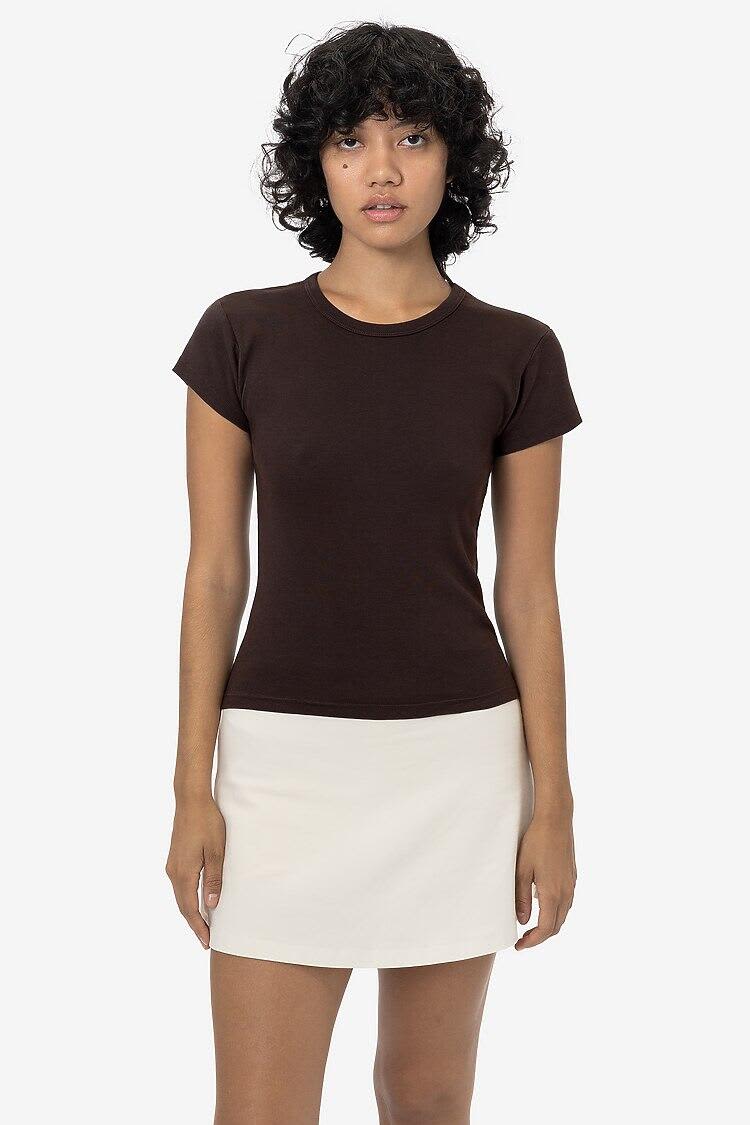 A brown cap sleeve baby tee displayed on a model, paired with a white skirt. The shirt has a subtle logo. Cap Sleeve Garment Dye Baby Tee - Image 1