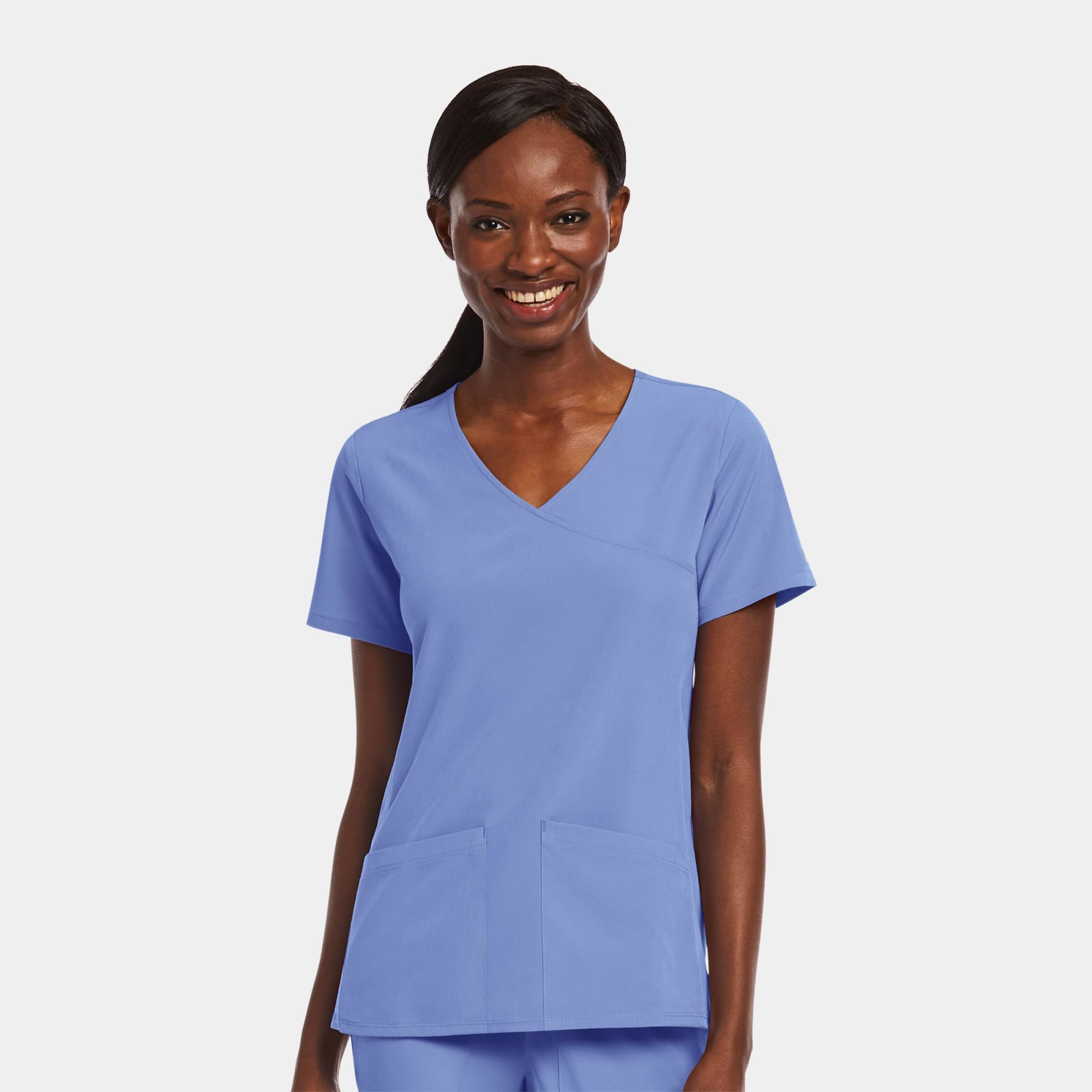 A womens mock wrap top in light blue with two front pockets and a V-neck design, featuring a branding logo. Matrix Impulse Womens Mock Wrap Top - Image 1