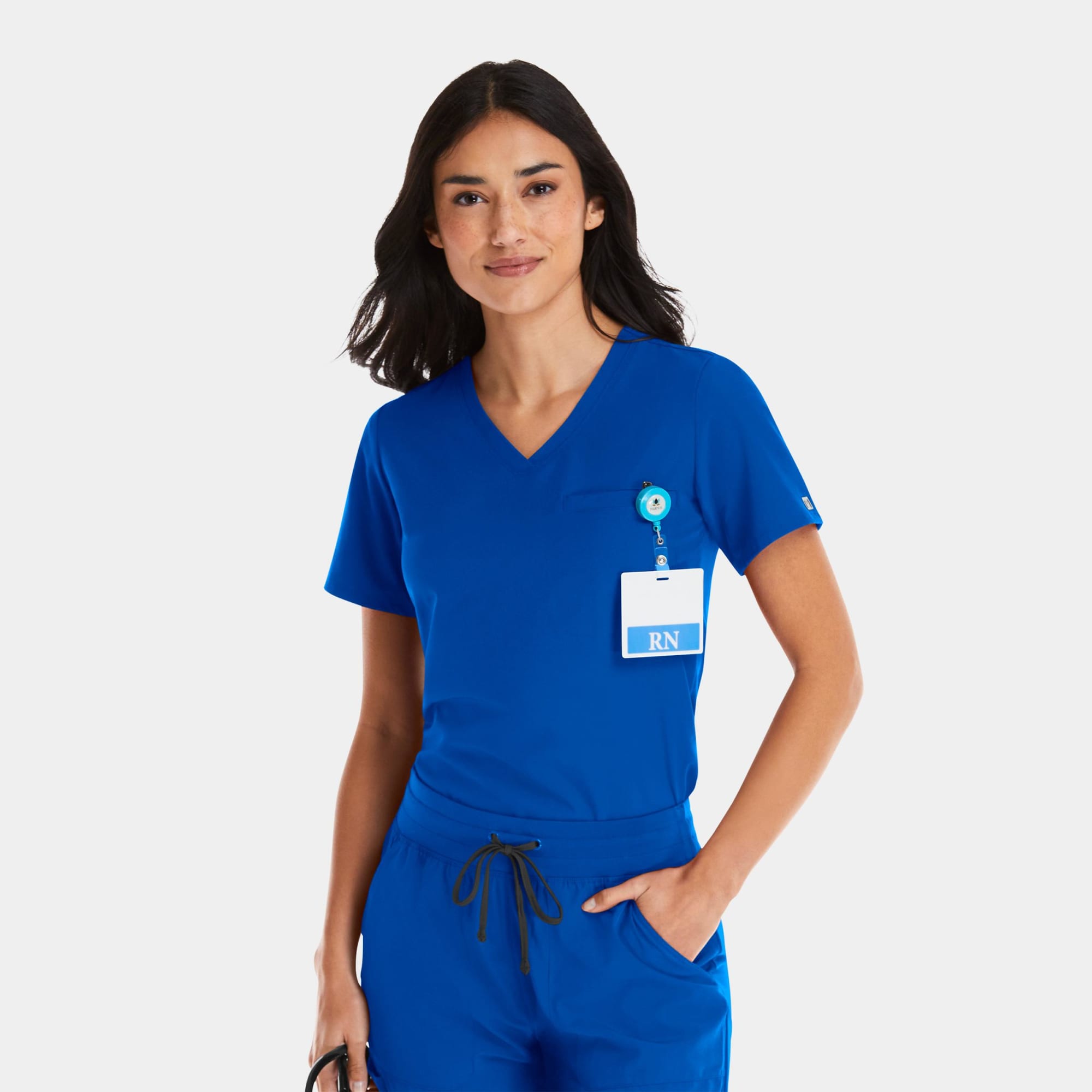 A woman wearing a bright blue V-neck top with a badge holder and black pants. The top has a logo. Matrix Impulse Womens Tuckable V-Neck Top - Image 1