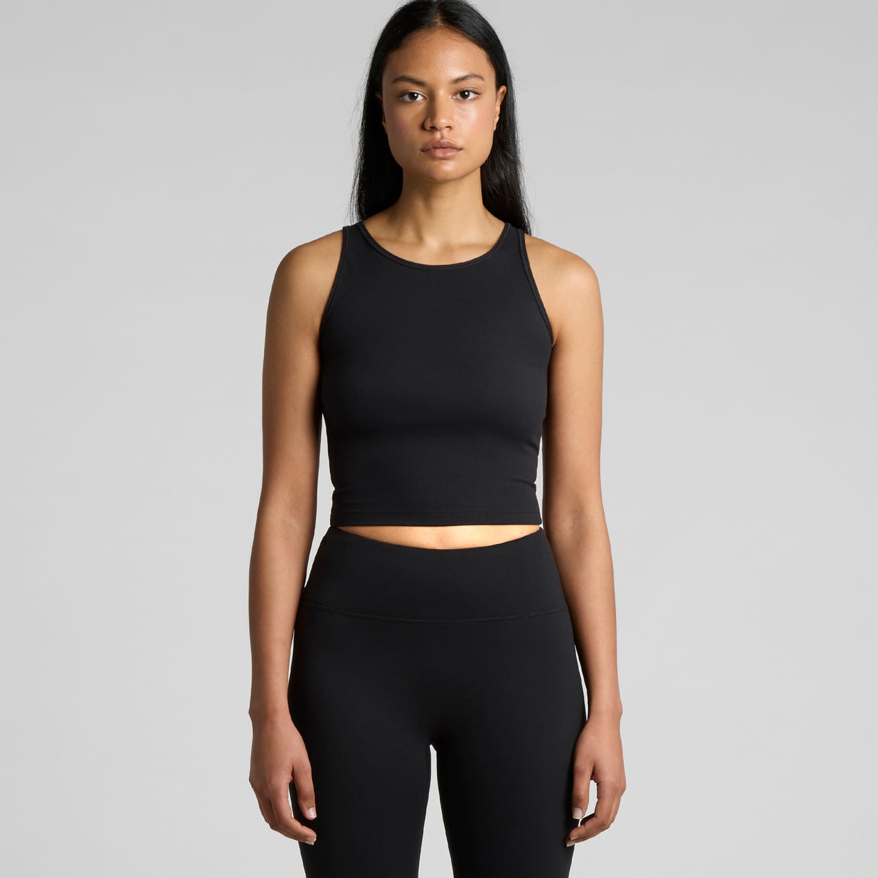 A black active crop tank top displayed on a model, featuring a form-fitting design and a subtle logo. Wo's Active Crop Tank - Image 1