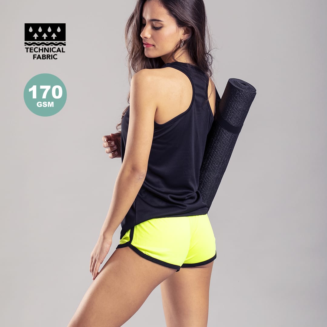 Bright neon yellow dress shorts with a black top, featuring a yoga mat rolled up against the side. Bizax Shorts - Image 1