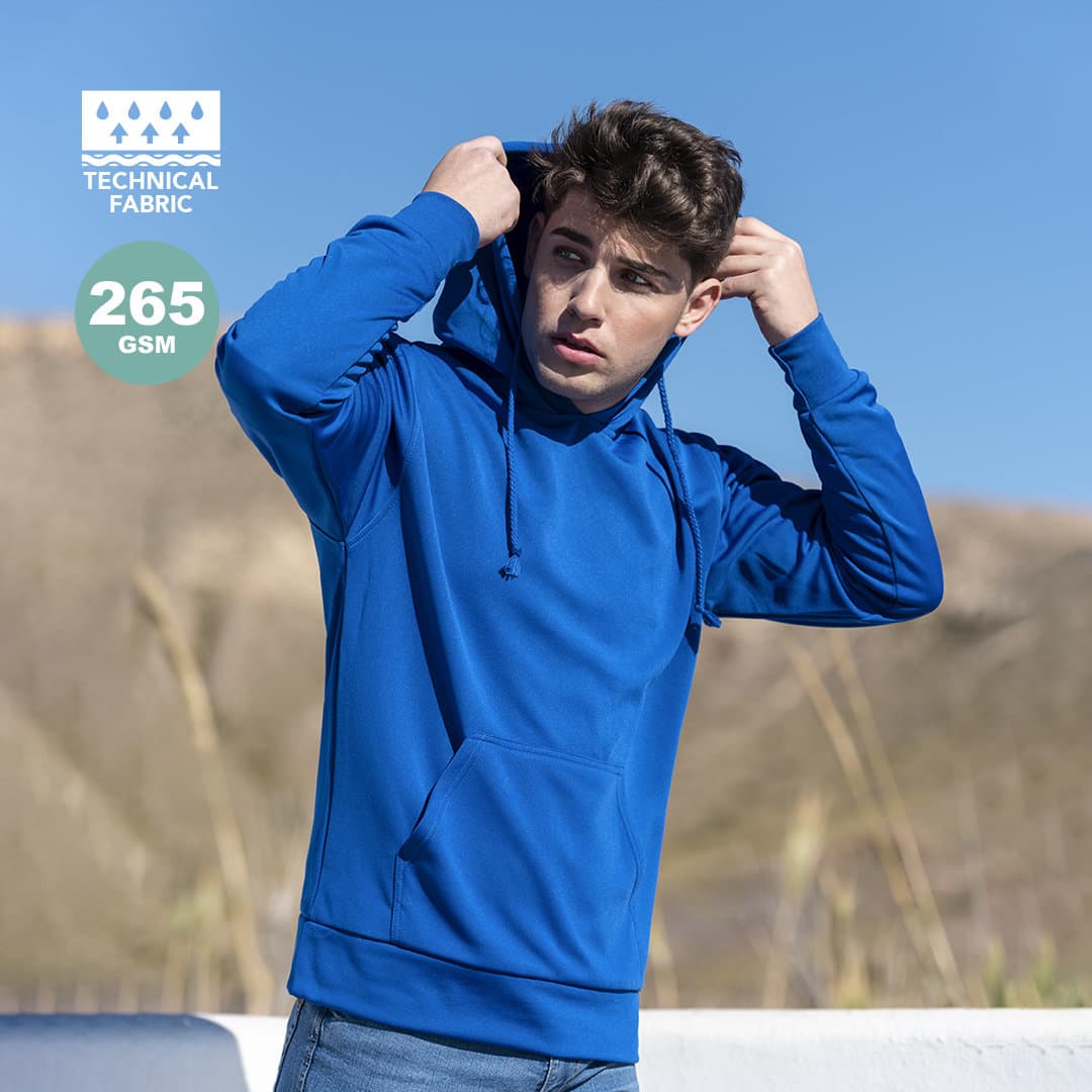 A blue technical sweatshirt with a hood, featuring a logo and worn by a person against a natural background. Theon Adult Technical Sweatshirt - Image 1