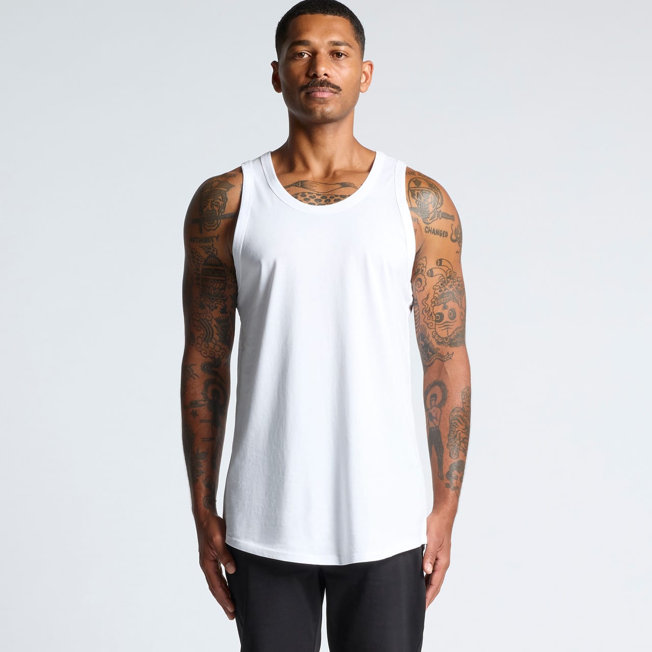 A white singlet worn by a model with tattoos, featuring a basic design and regular fit. It has a logo. Authentic Singlet - Image 1
