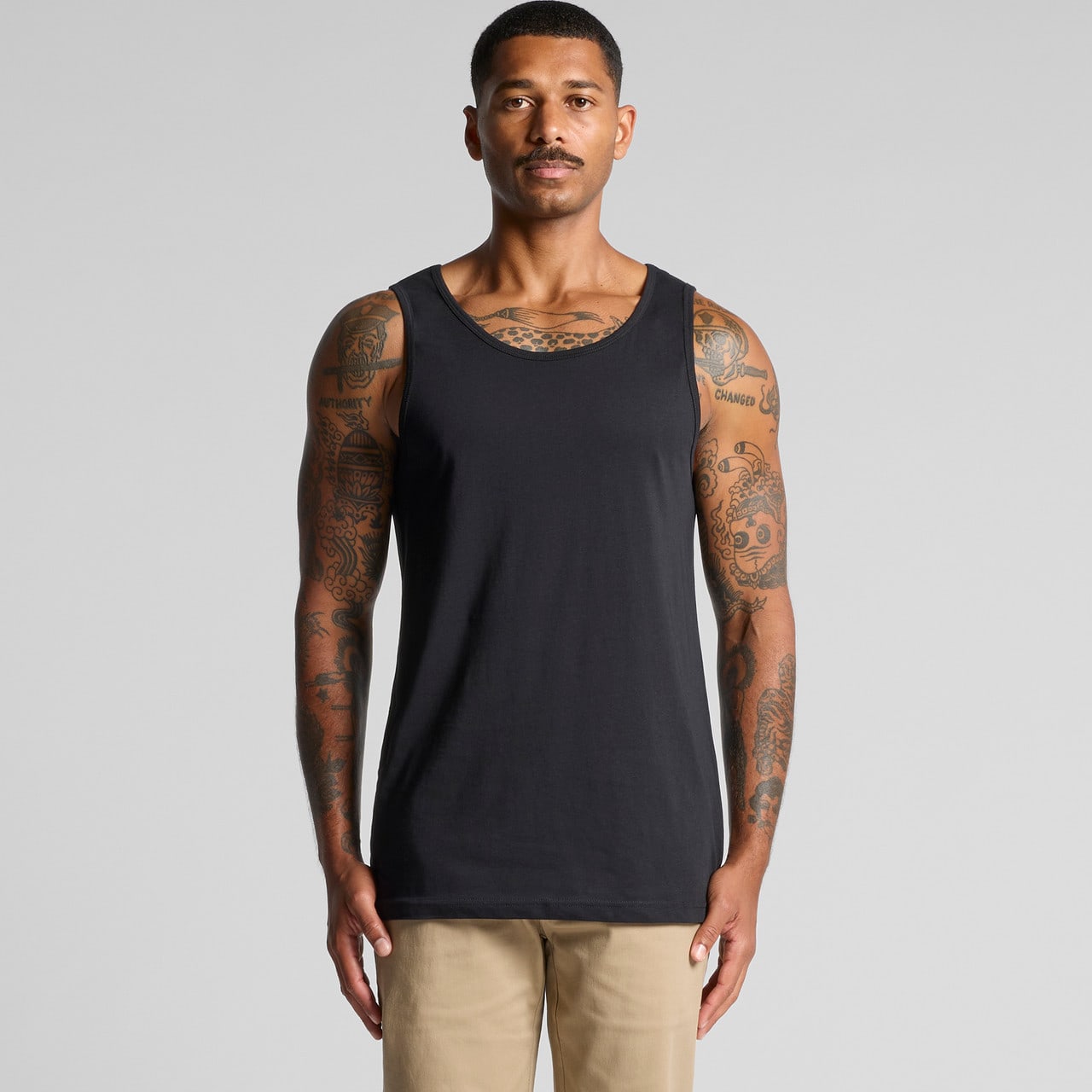 A man stands wearing a plain black singlet, showcasing its simple design and fit. The singlet has a logo. Lowdown Singlet - Image 1