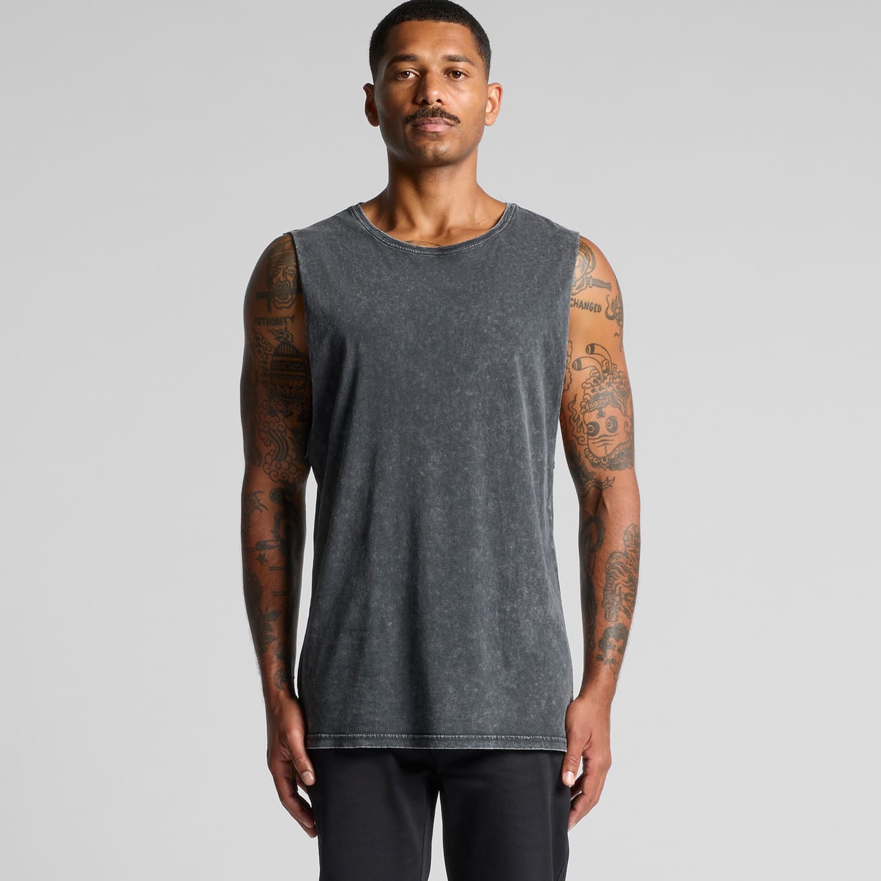 A sleeveless, stone wash tank in dark grey worn by a model. The tank features a logo. Stone Wash Barnard Tank - Image 1